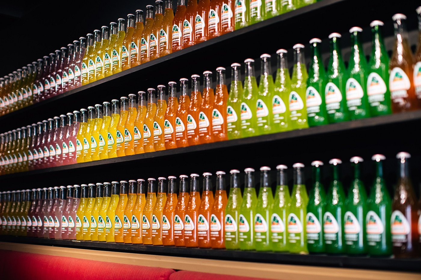 Several shelves displaying rows of colorful bottles of hot sauce in red, yellow, orange, and green flavors.