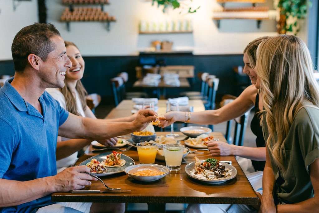 People sitting at a restaurant table, smiling, sharing food and drinks