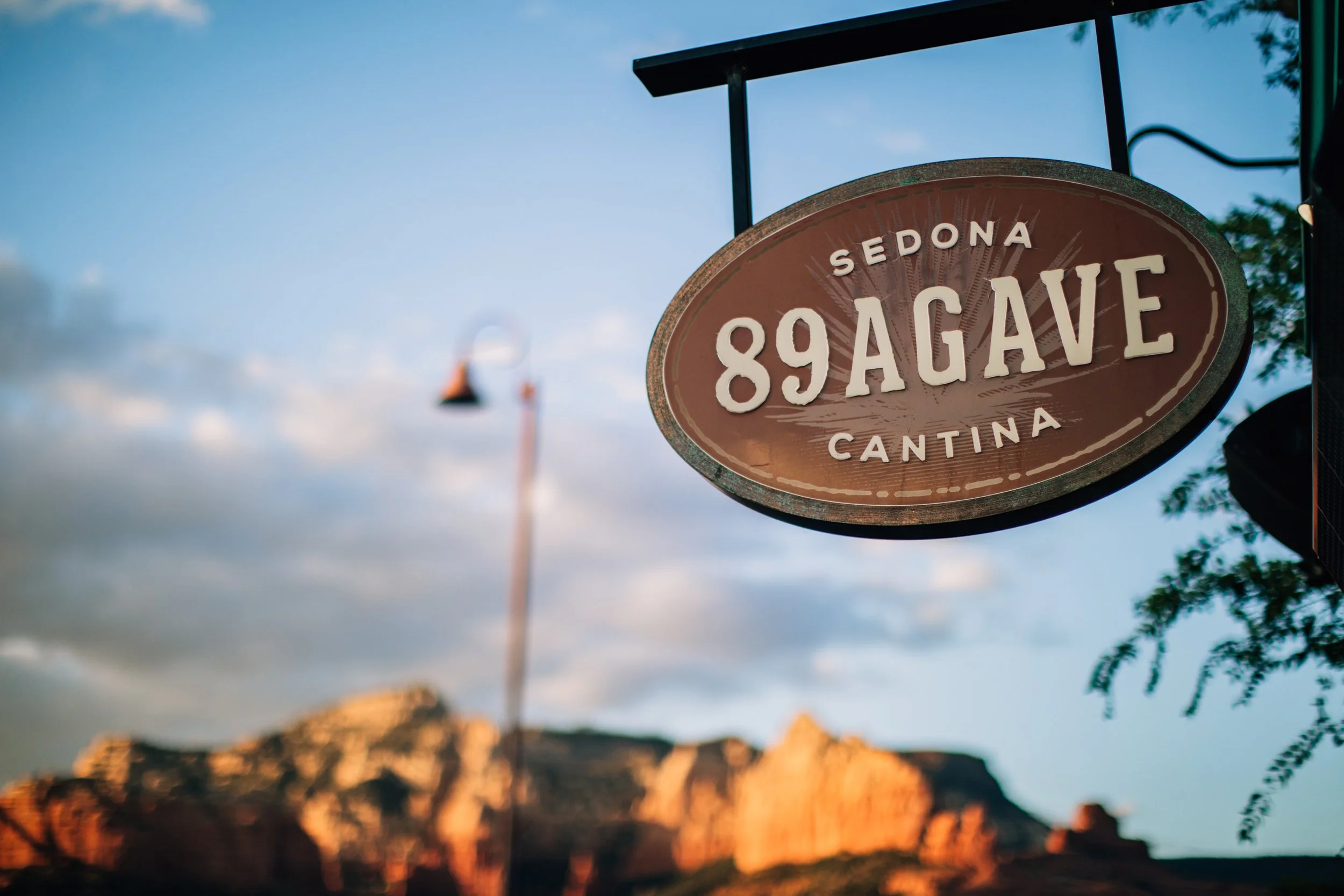 A street sign for 89 Agave in Sedona, Arizona, with a rocky landscape and sunset in the background.