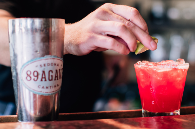 Bartender garnishing a vibrant pink cocktail with a lime wedge behind a bar counter.