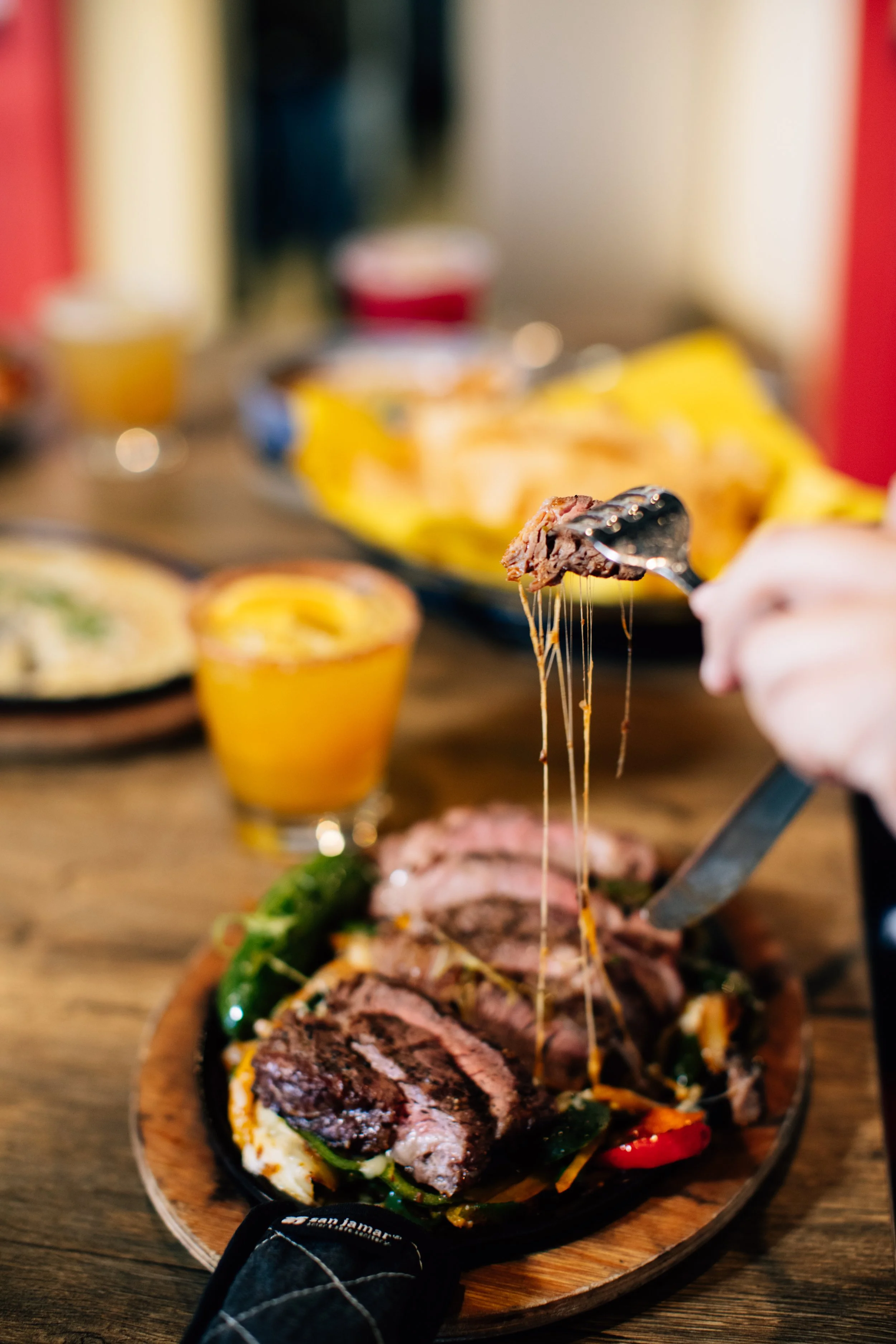 Person cutting into a sizzling steak on a cast iron skillet with cheese and peppers
