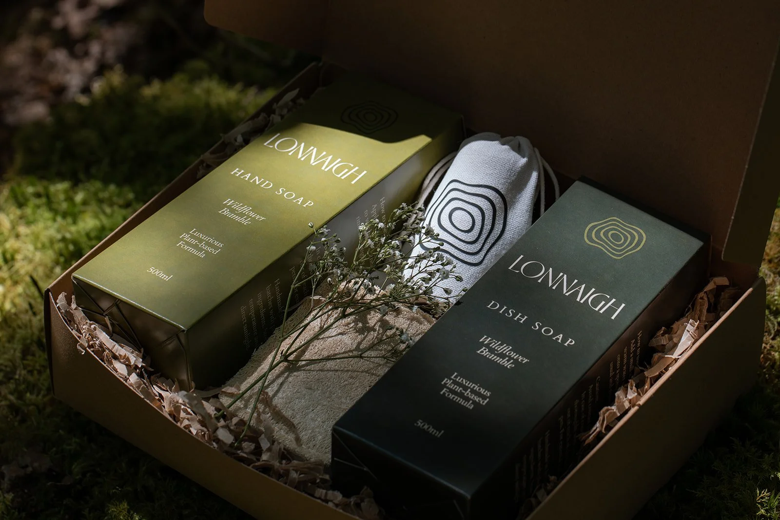Open gift box containing two boxes of LONWIGH soap, one green and one black, with a small cloth bag and a sprig of flowers inside.