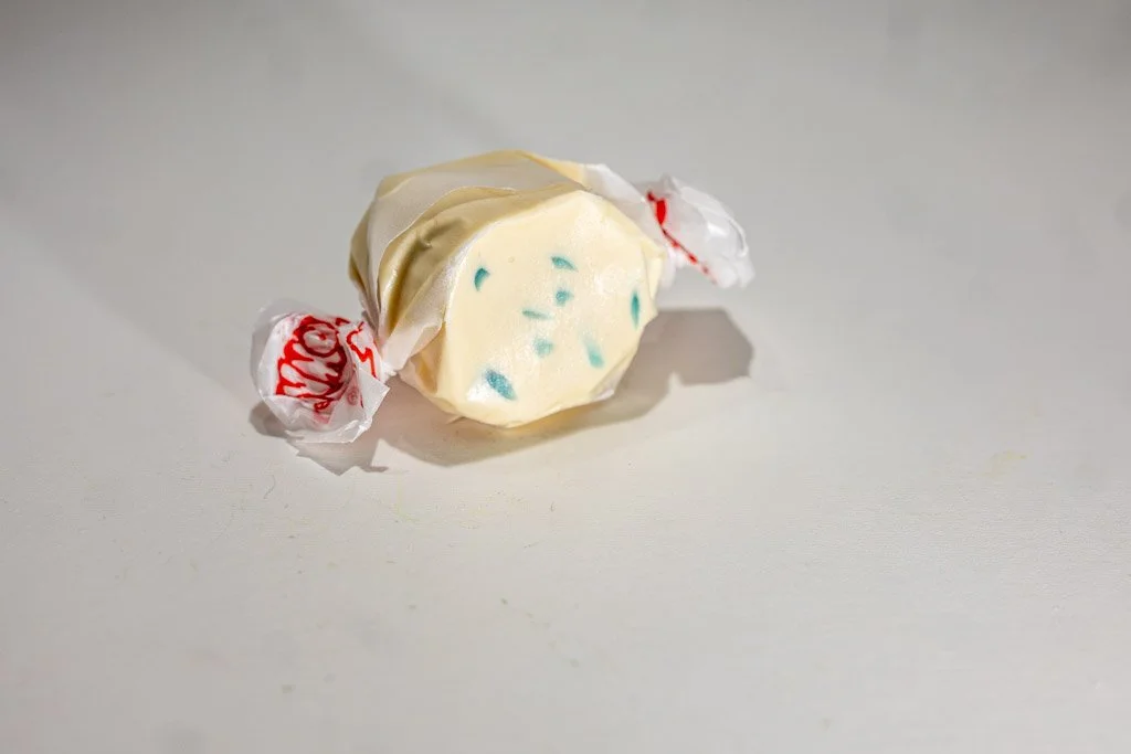 Blueberry muffin flavored taffy in clear wrapper with red lettering on the ends. a soft cream colored taffy piece with blue specks sprinkled on the inside.