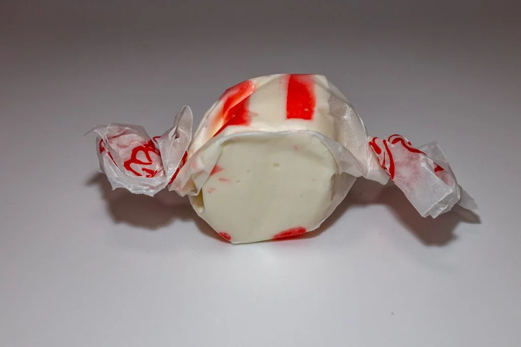 Peppermint flavored taffy in clear wrapper with red lettering. a white, minty piece with red stripes on the outside.