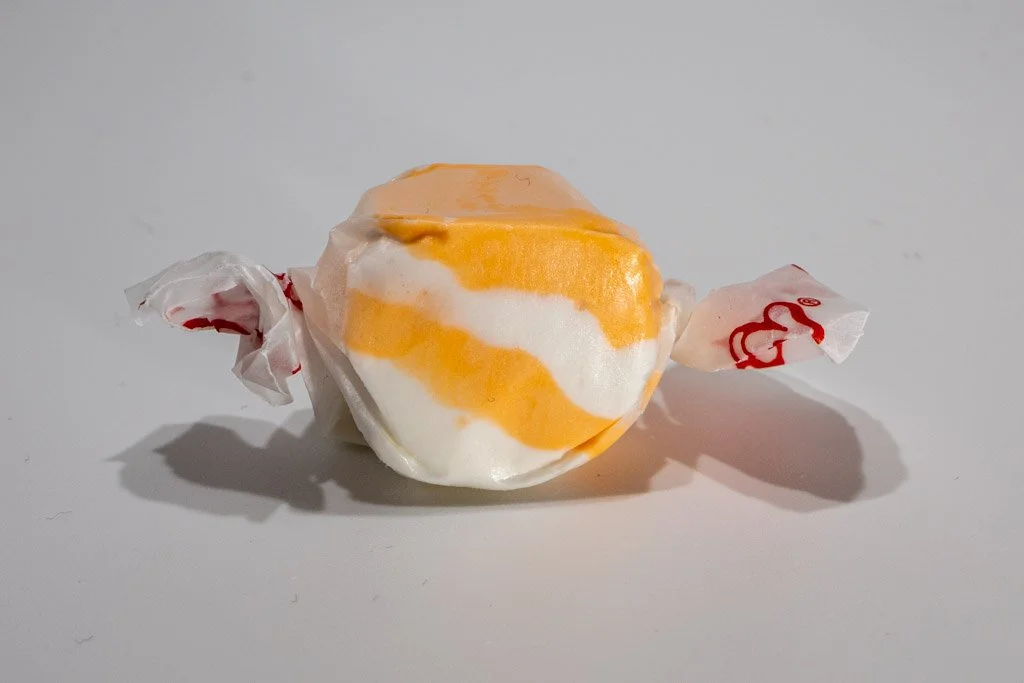 Orange and white striped peaches ‘n cream saltwater taffy from Sea Bird Gifts & Candy in Westport WA. Creamy peach-flavored taffy wrapped in wax paper with red print