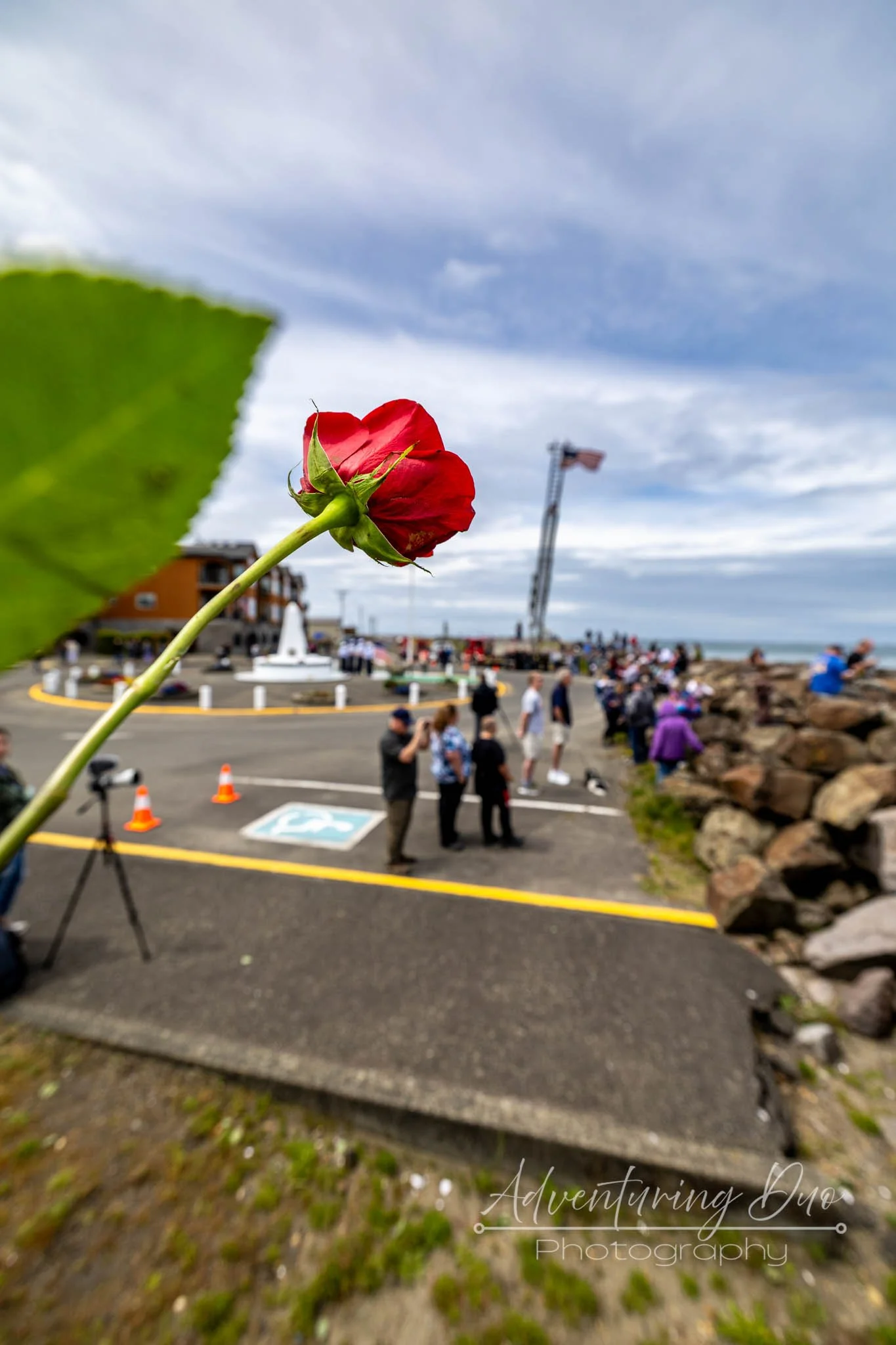 Red rose held in the foreground during the Day of Remembrance and Blessing of the Fleet ceremony in Westport, Washington, with community members gathered near the marina before Memorial Day.