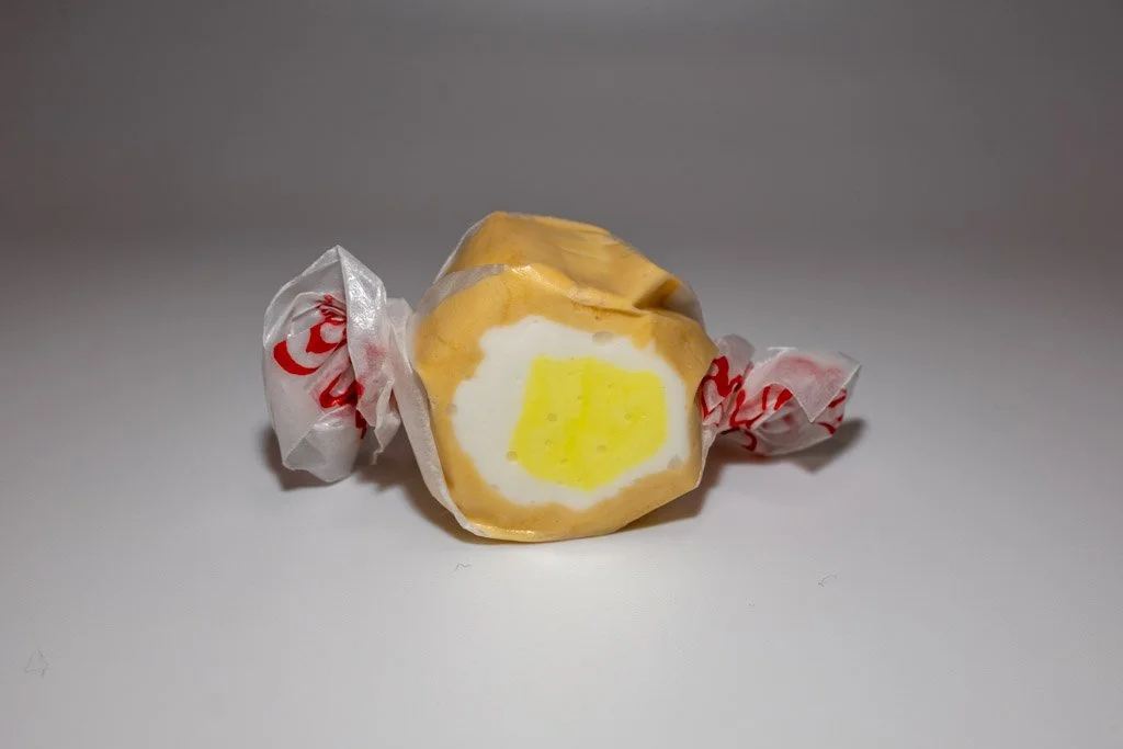 Banana Cream Pie flavored taffy in clear wrapper with red lettering on the ends. soft orange taffy on the outside with white and yellow on the inside.