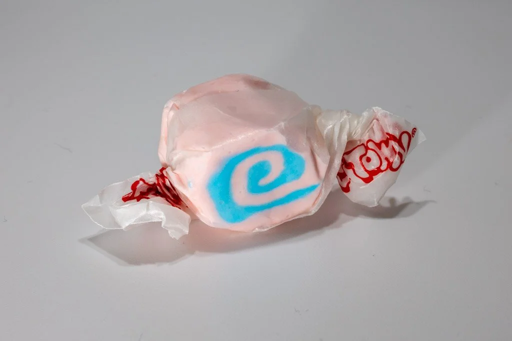 A salt water taffy piece with a soft pink exterior and a bright sky-blue swirl in the center. Wrapped in clear wax paper with red branding.