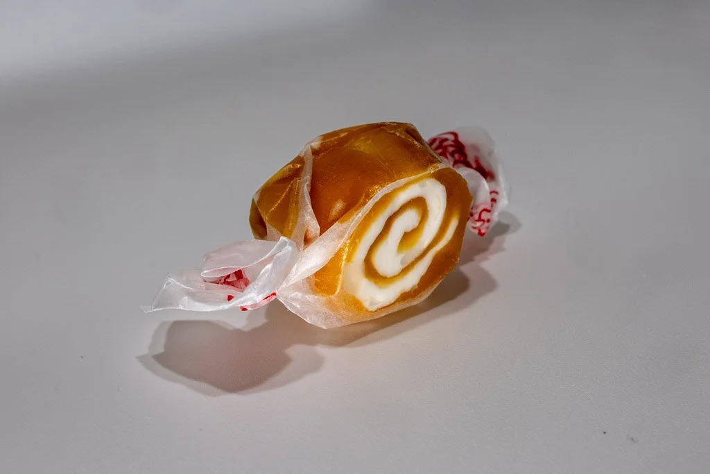 caramel swirl taffy in clear wrapped and red lettering on the ends. a opaque tan color swirled with cream.