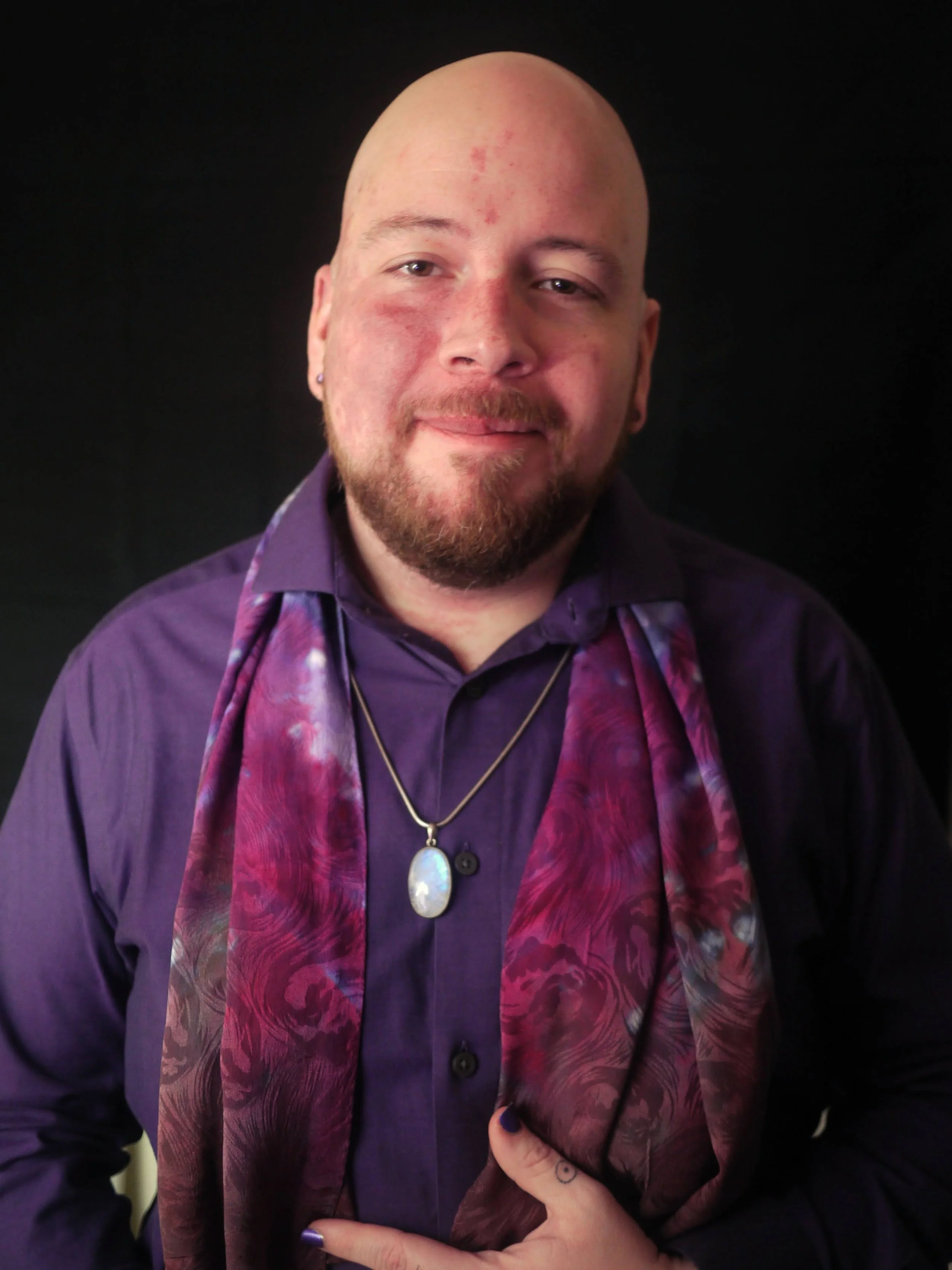 Portrait of Laurent, a non-binary person with pale skin, a red facial birthmark and facial hair, wearing a purple shirt and scarf, with a moonstone necklace