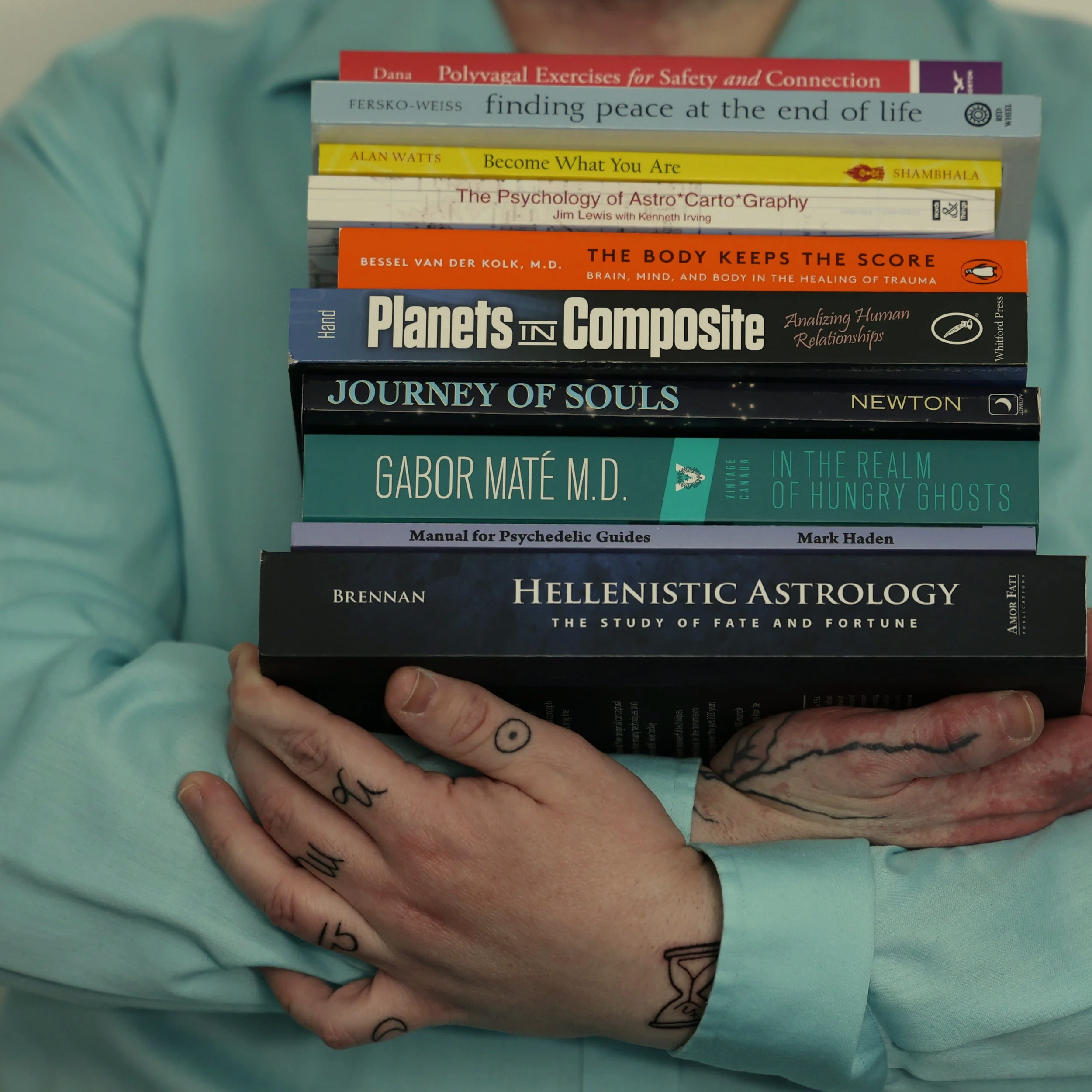 Laurent's hands with astrology tattoos, holding a stack of books