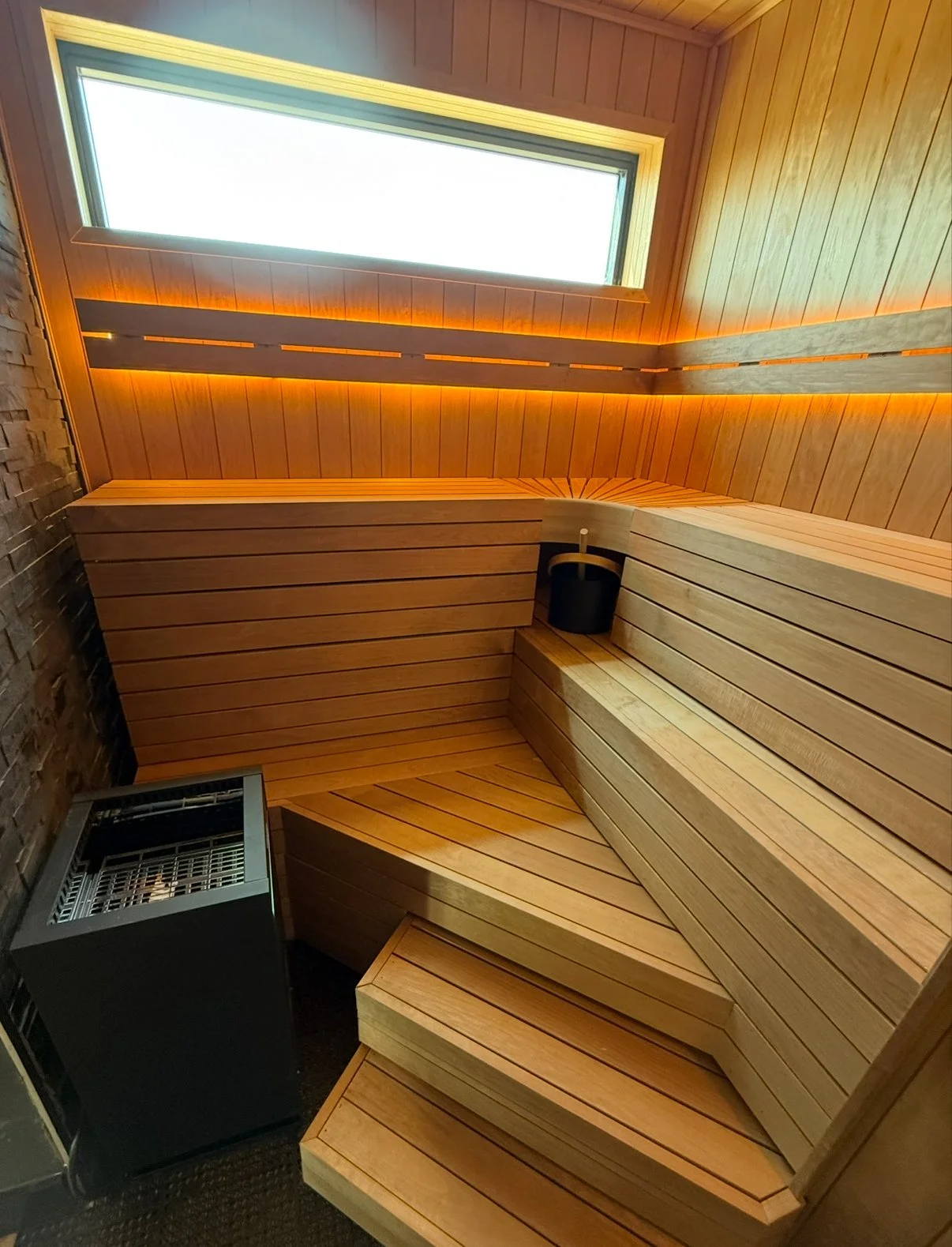 Interior view of a wooden sauna with bench seating, a window, and ambient lighting.
