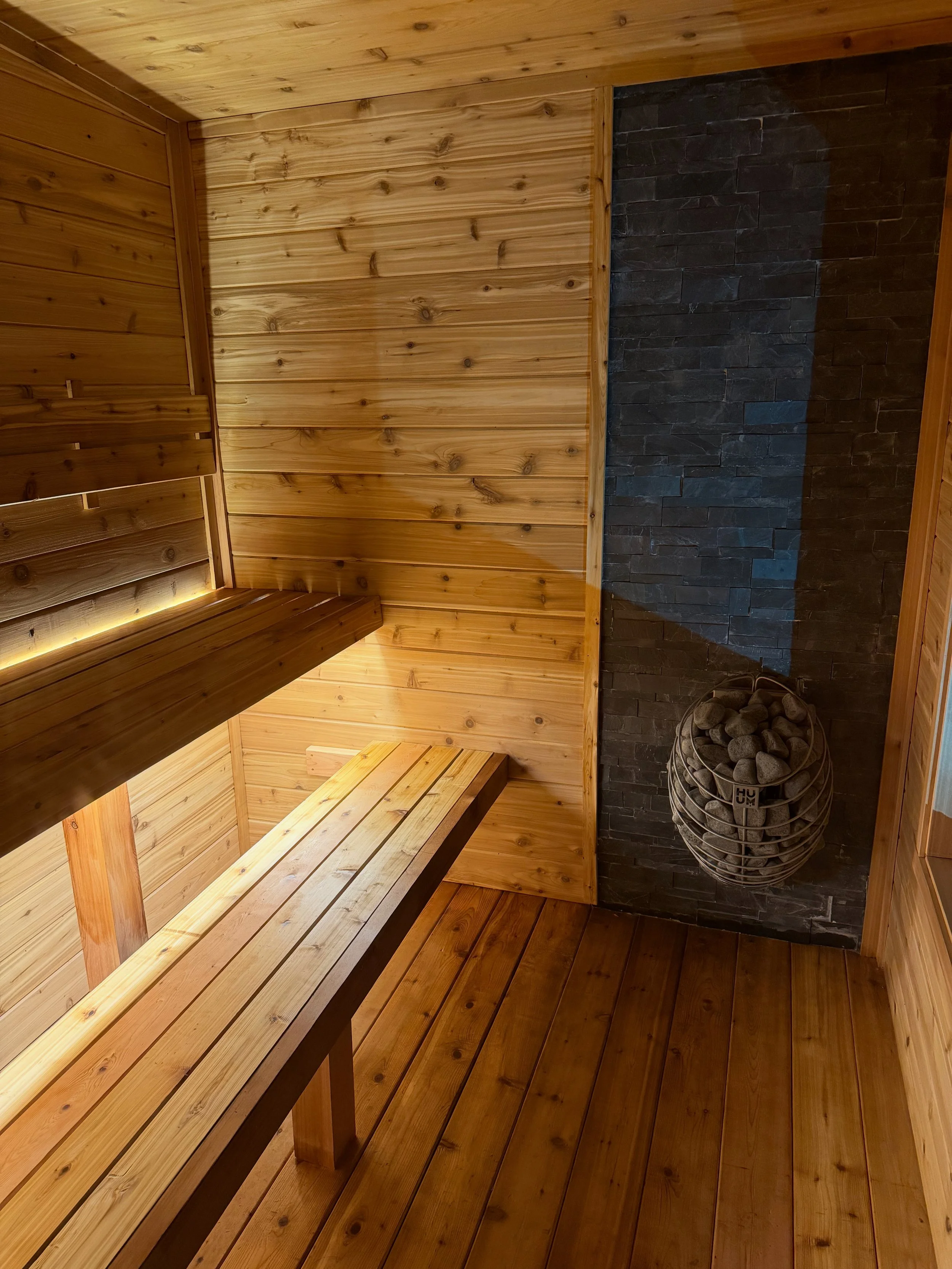 Wood-paneled sauna interior with tiered benches and a stone sauna heater