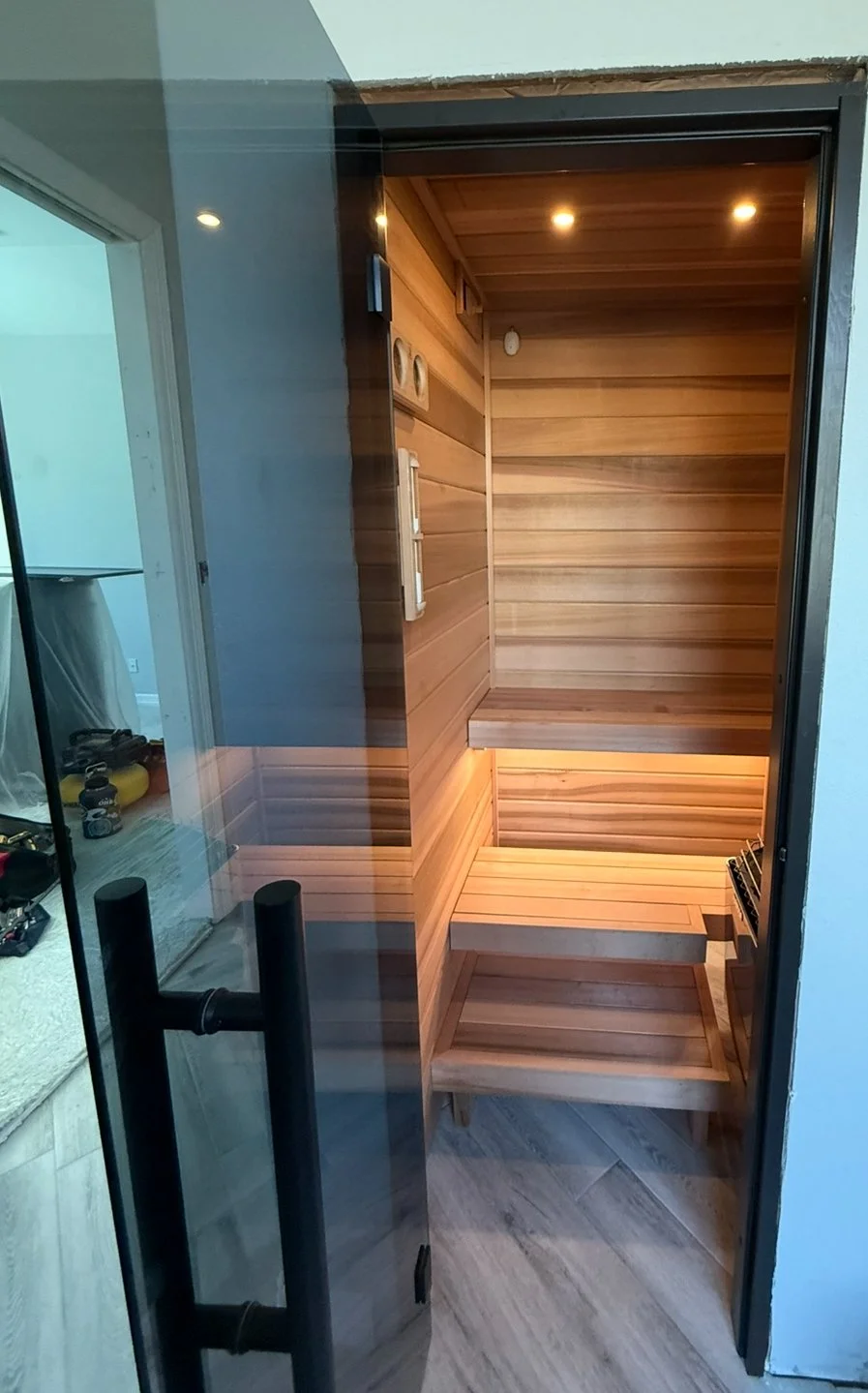 Inside a small, modern steam room or sauna with wooden paneling, seating benches, and a heater in the corner.