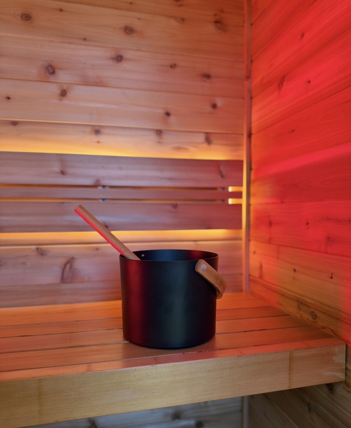 Black sauna bucket with wooden ladle inside a warmly lit wooden sauna