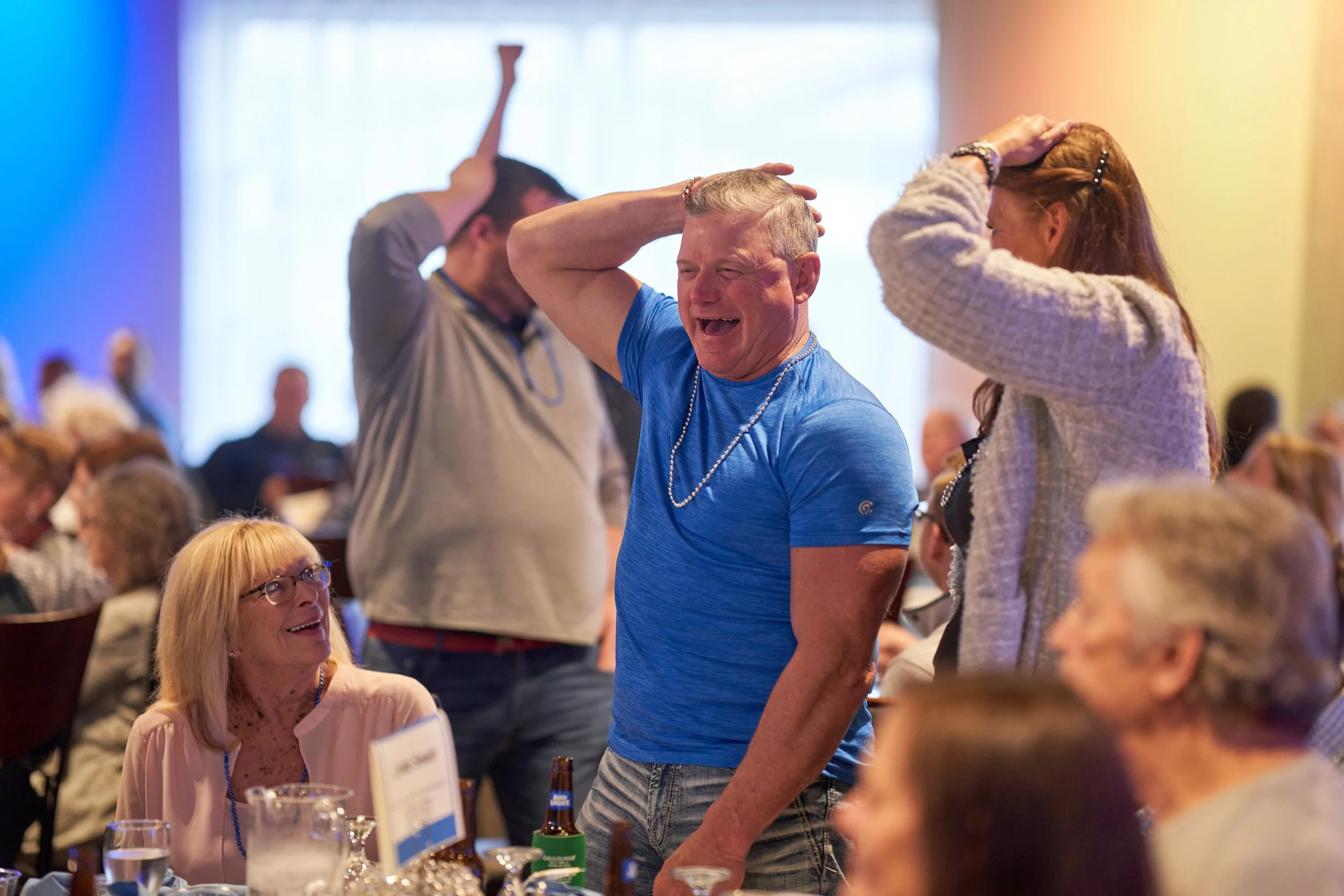 People in a lively setting, laughing and holding their heads, suggesting a fun or game activity.