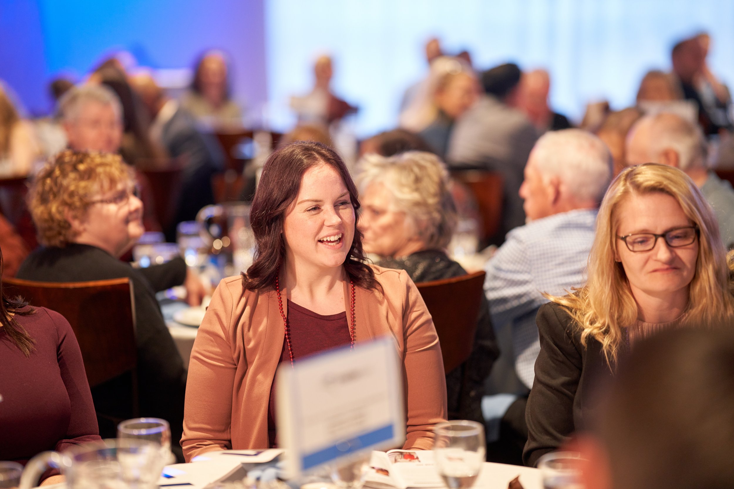 People at a formal event, seated at tables, conversing and smiling.