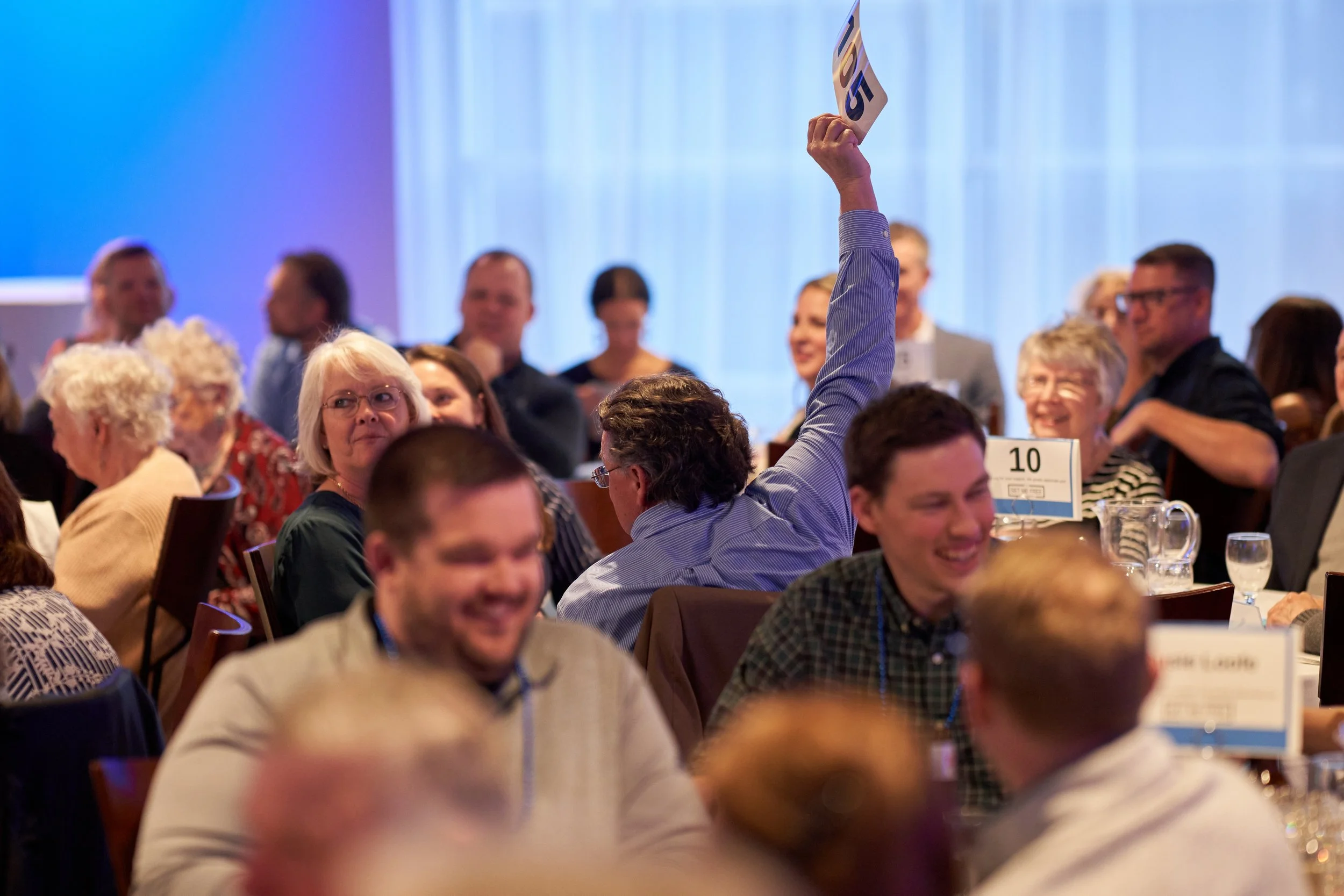 People attending an indoor event, with a man holding up a bidding number.