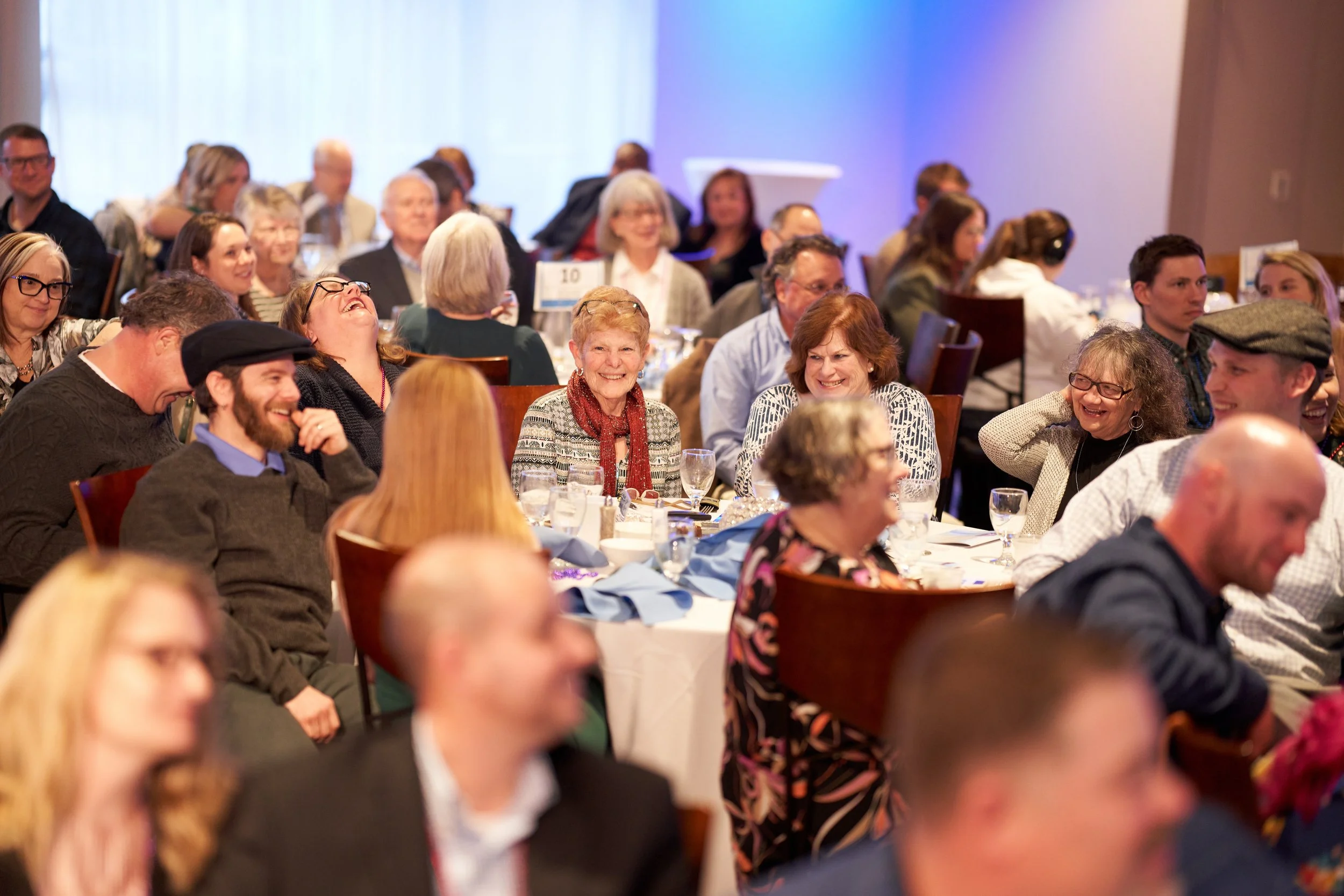 People seated at round tables, smiling and laughing at an event.