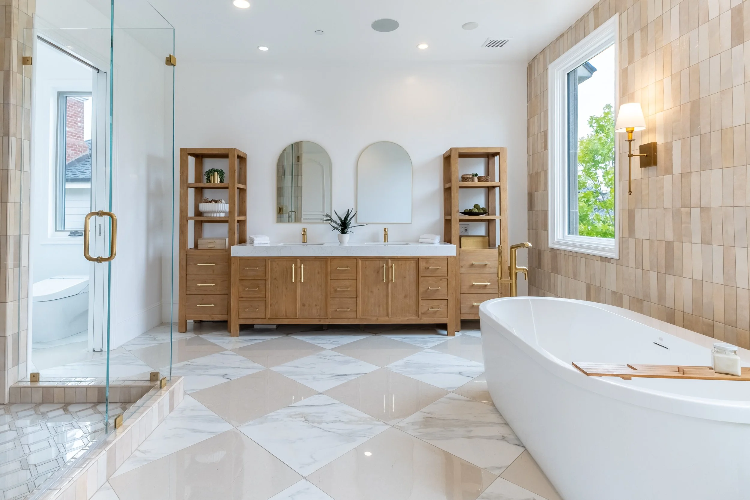 Modern bathroom with a white freestanding bathtub, a wooden vanity with two mirrors, tile wall with window, and a glass shower enclosure.