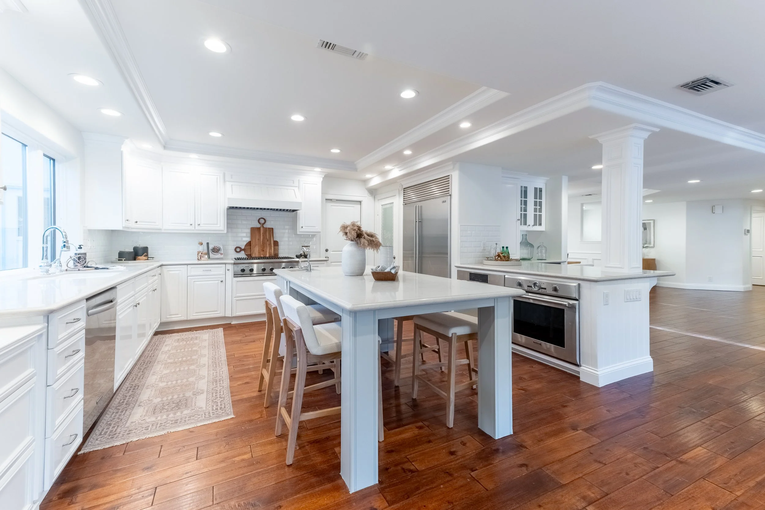 Bright, modern kitchen with white cabinets, stainless steel appliances, a large island with seating, and hardwood floors.