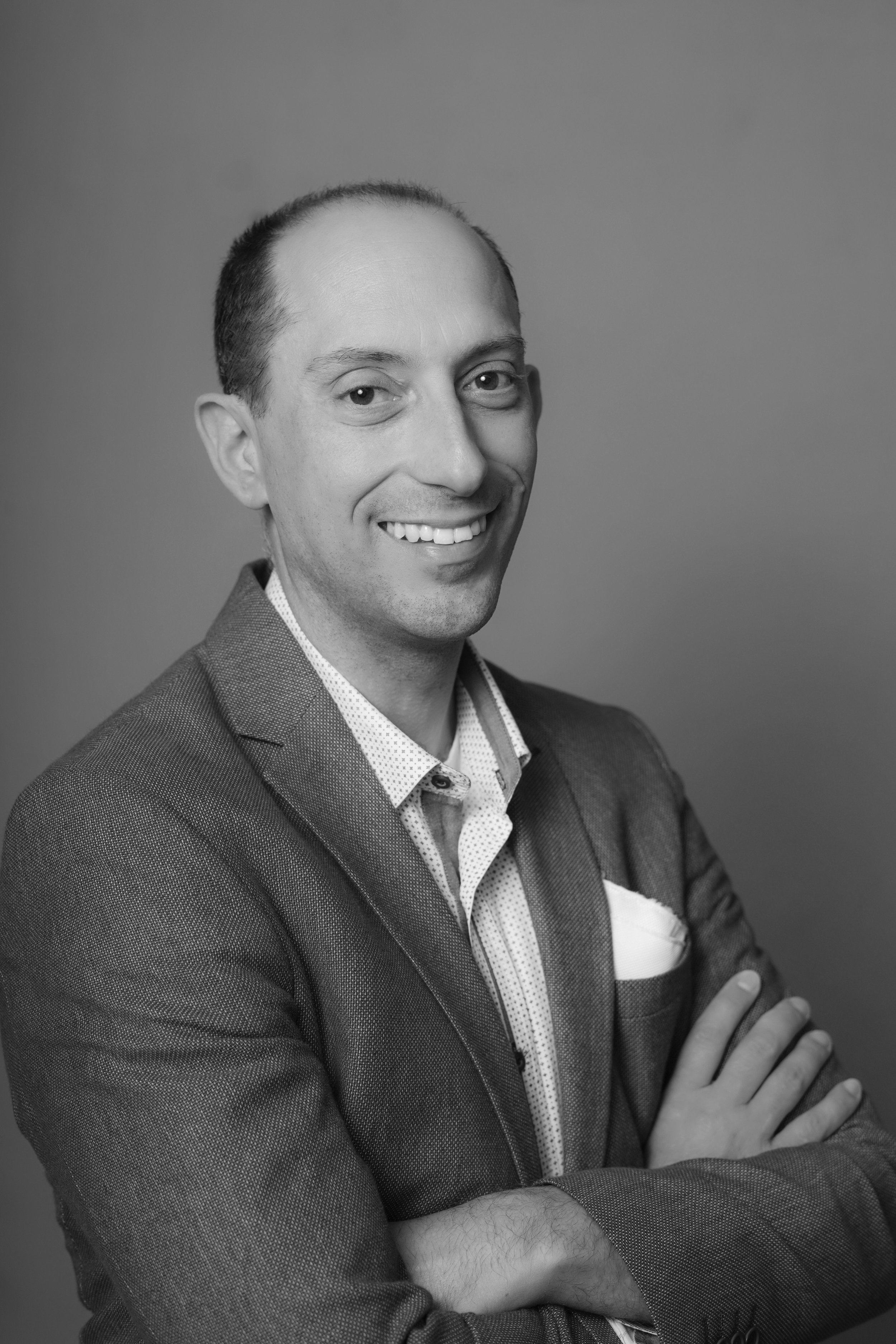 Black and white portrait of a smiling man in a suit, arms crossed.