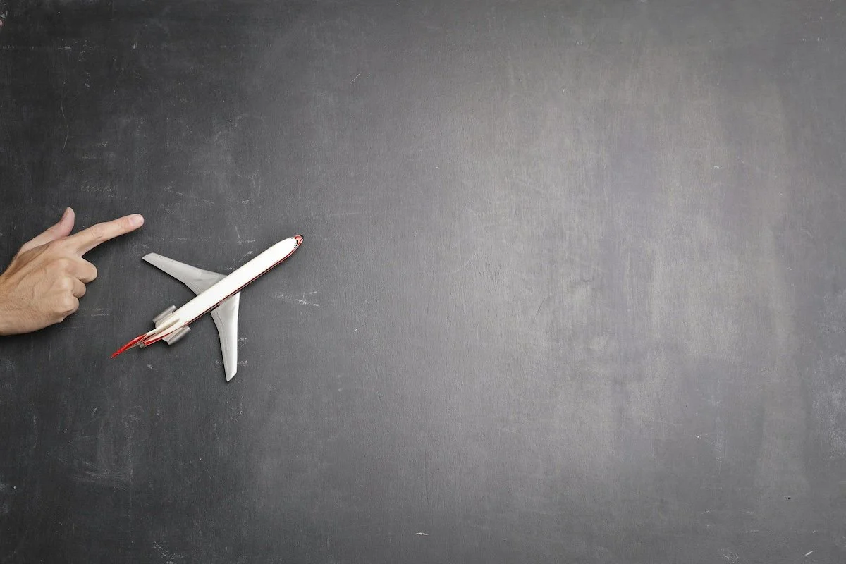 A chalkboard with a toy airplane on it and a hand with a finger pointing the way for the plane.