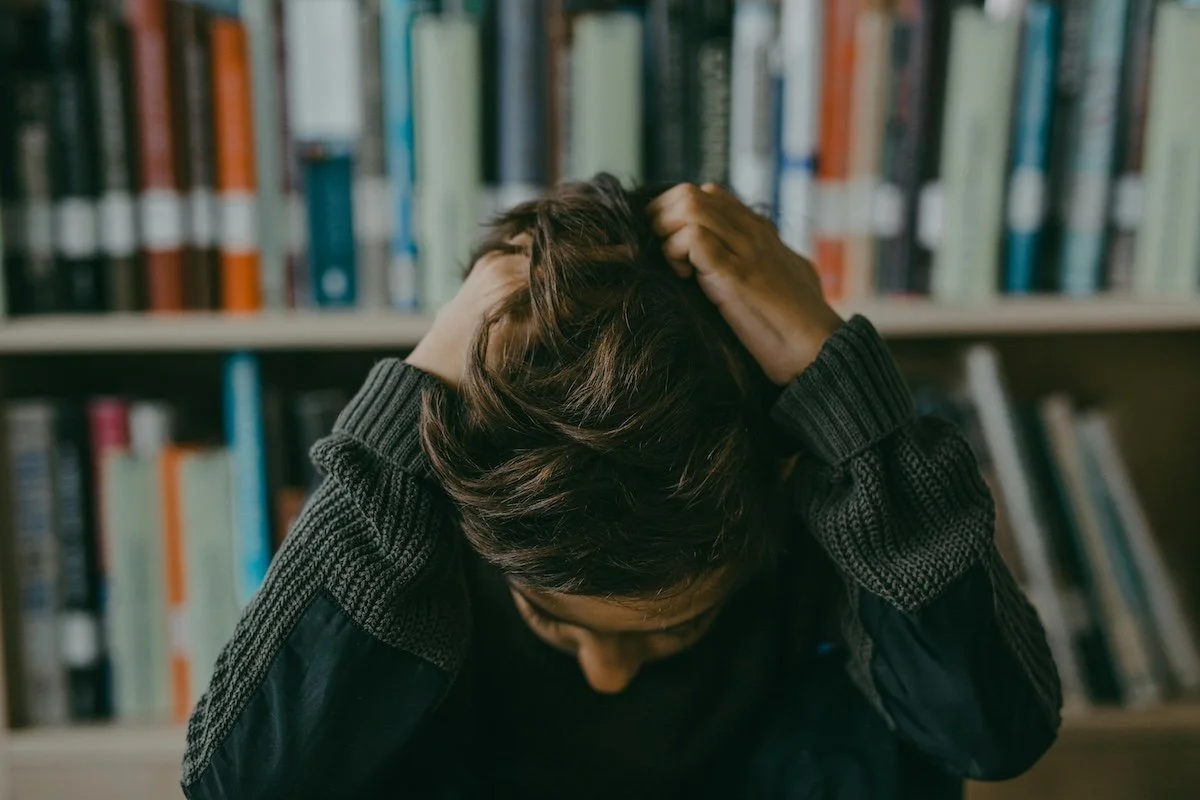 A frustrated boy at a desk with his head in his hands.