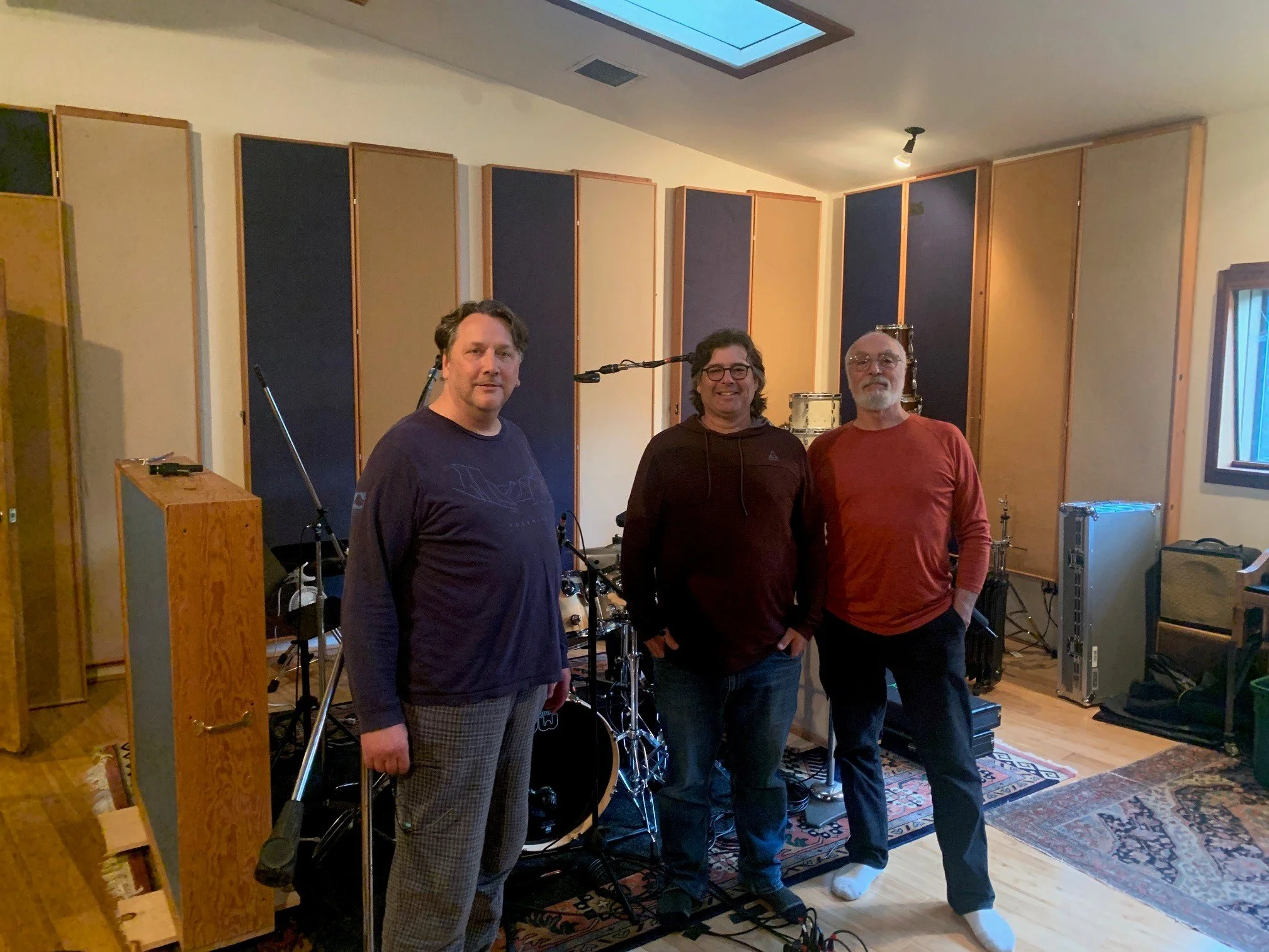 Three men standing in a recording studio with musical equipment and acoustic panels.