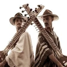 Two members of the band Raganova wearing wide-brimmed hats and ponchos, holding sitars crossed behind their backs.