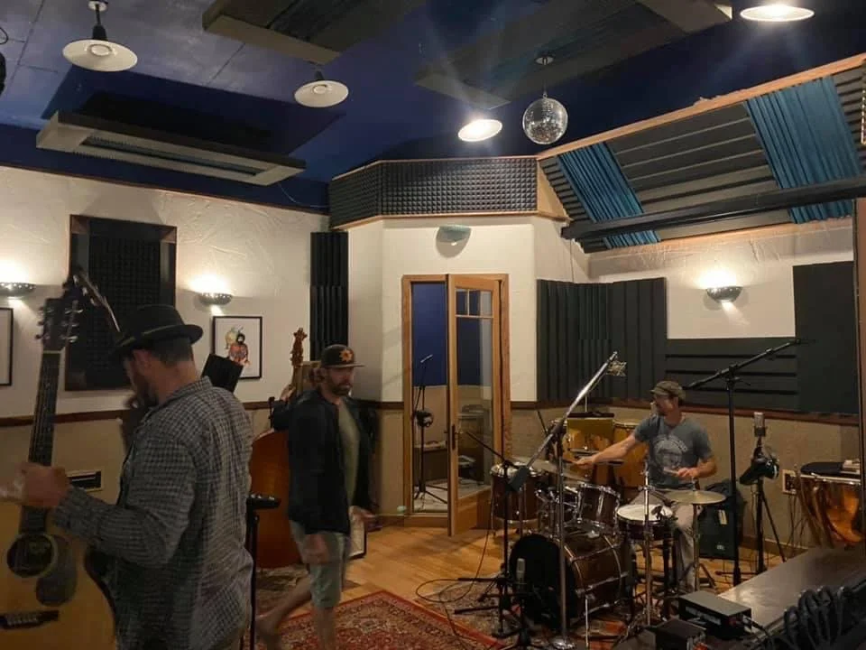 Musicians in a recording studio with instruments and soundproofing panels.