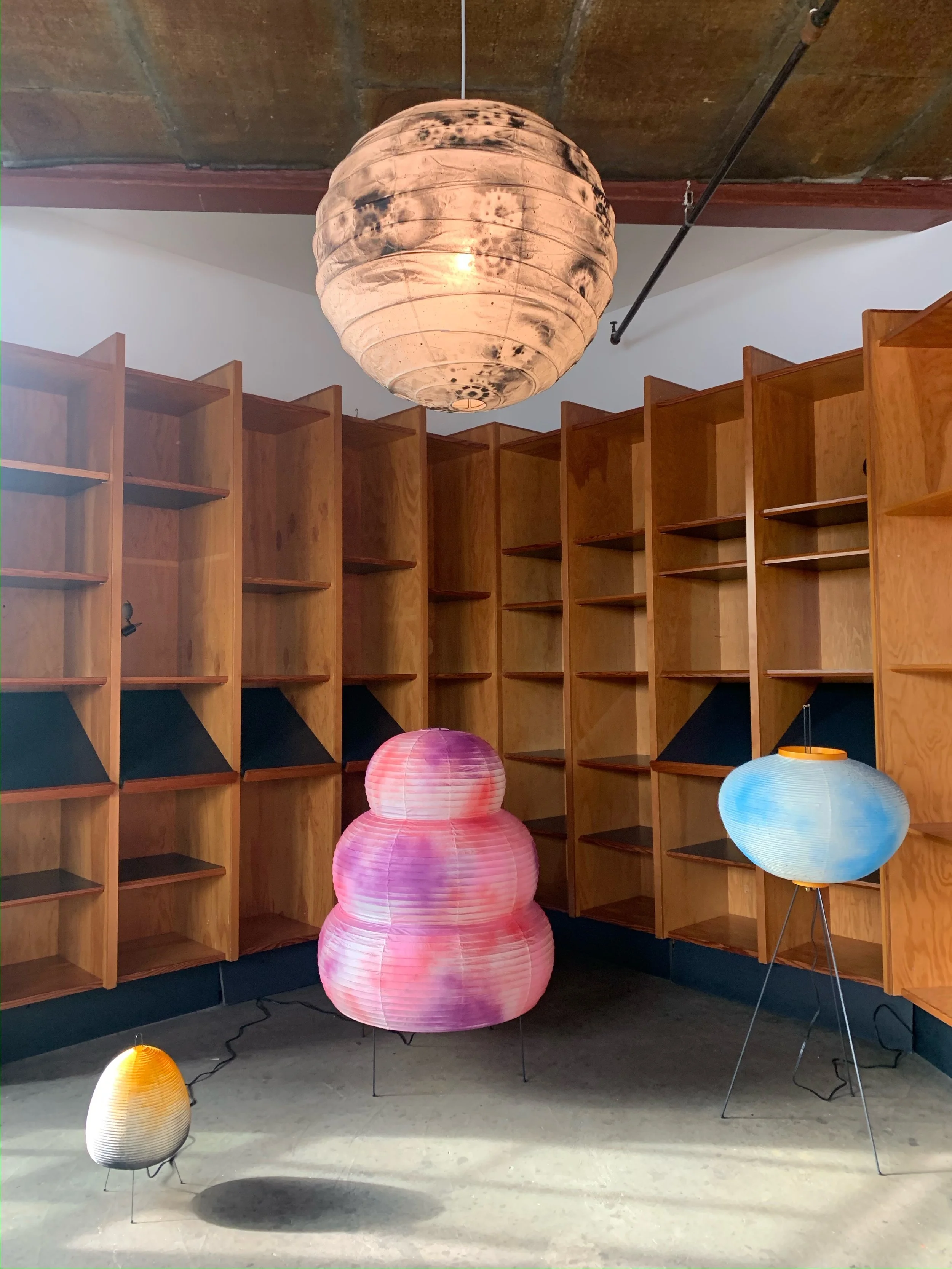 Various colored paper lanterns hanging in front of wooden bookshelves and a white wall.