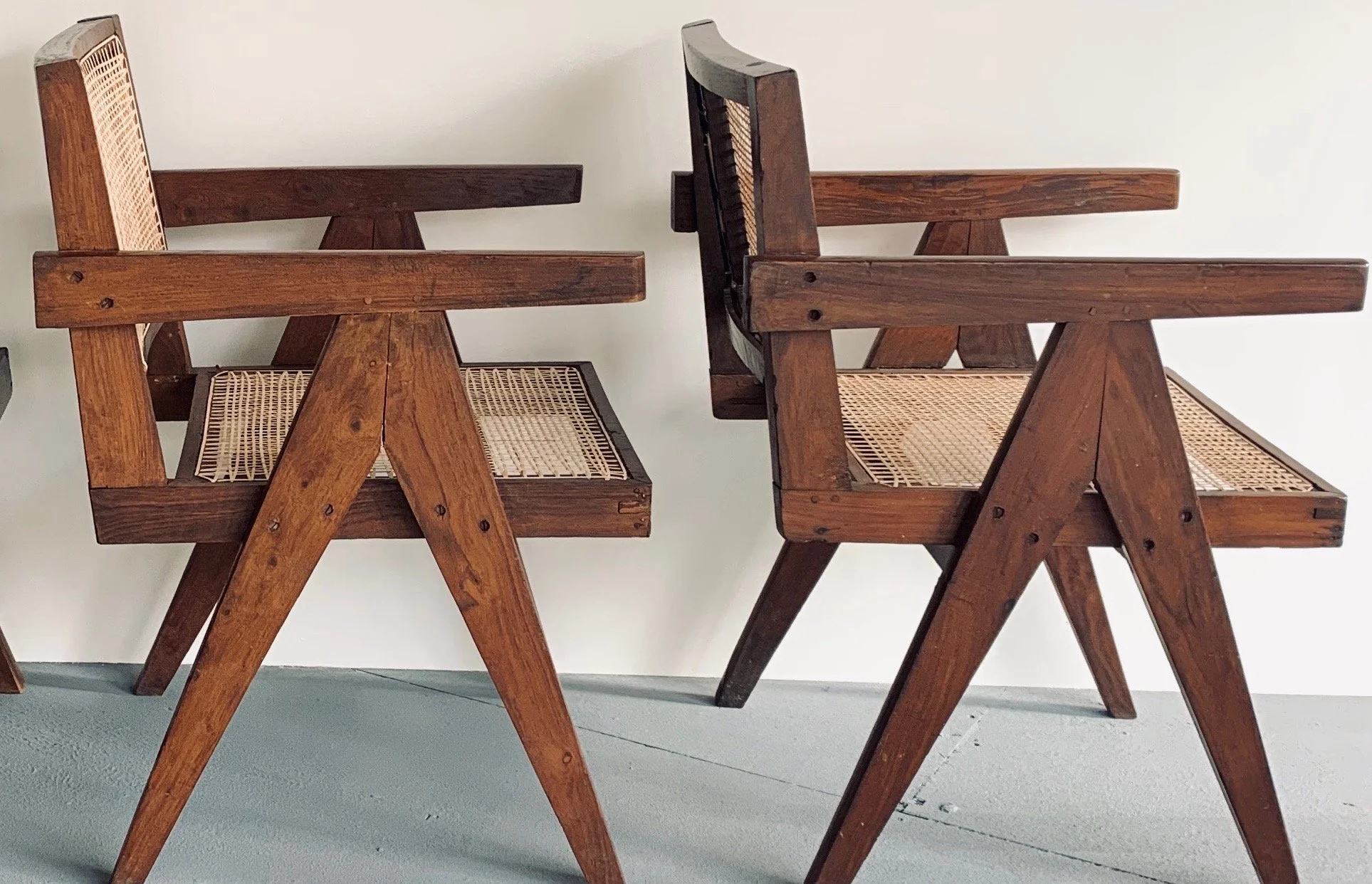 Two wooden chairs with woven cane seats and backs, positioned upside down and resting on a flat surface against a plain wall.