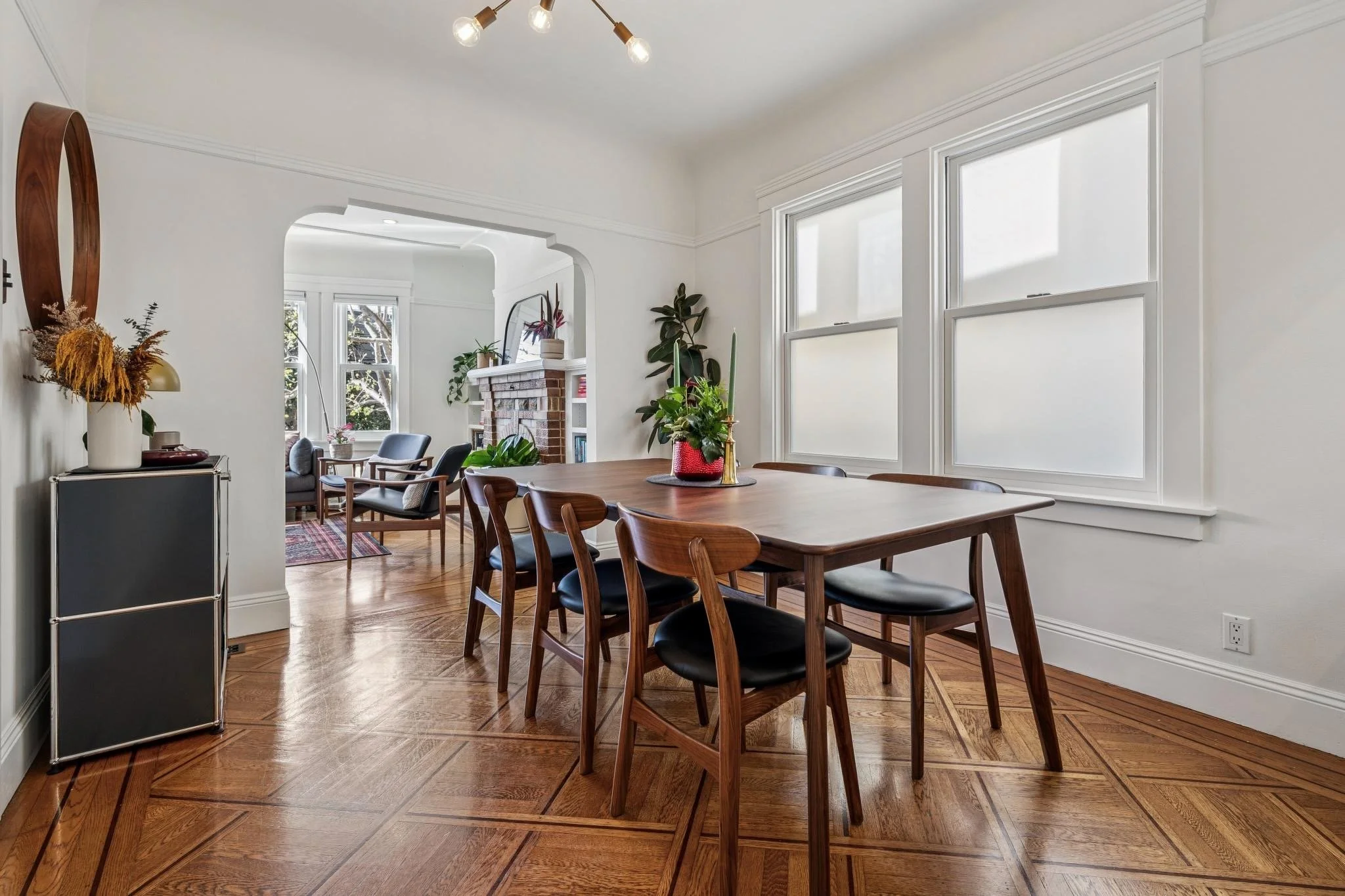 Dining room with wooden table, black cushioned chairs, large windows, and a plant centerpiece.