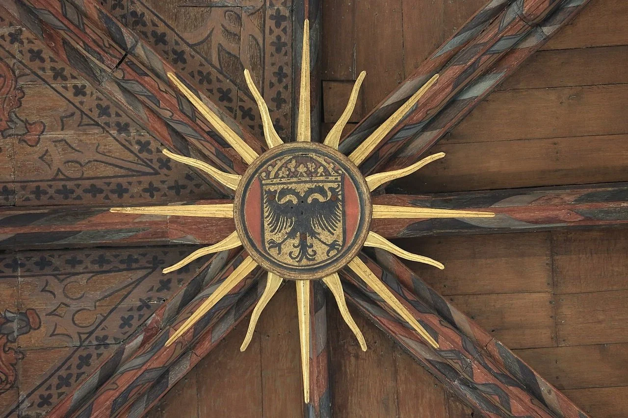 Wooden ceiling with painted beams and a decorative shield featuring a black eagle with its wings spread, crowned, on a red and gold background.