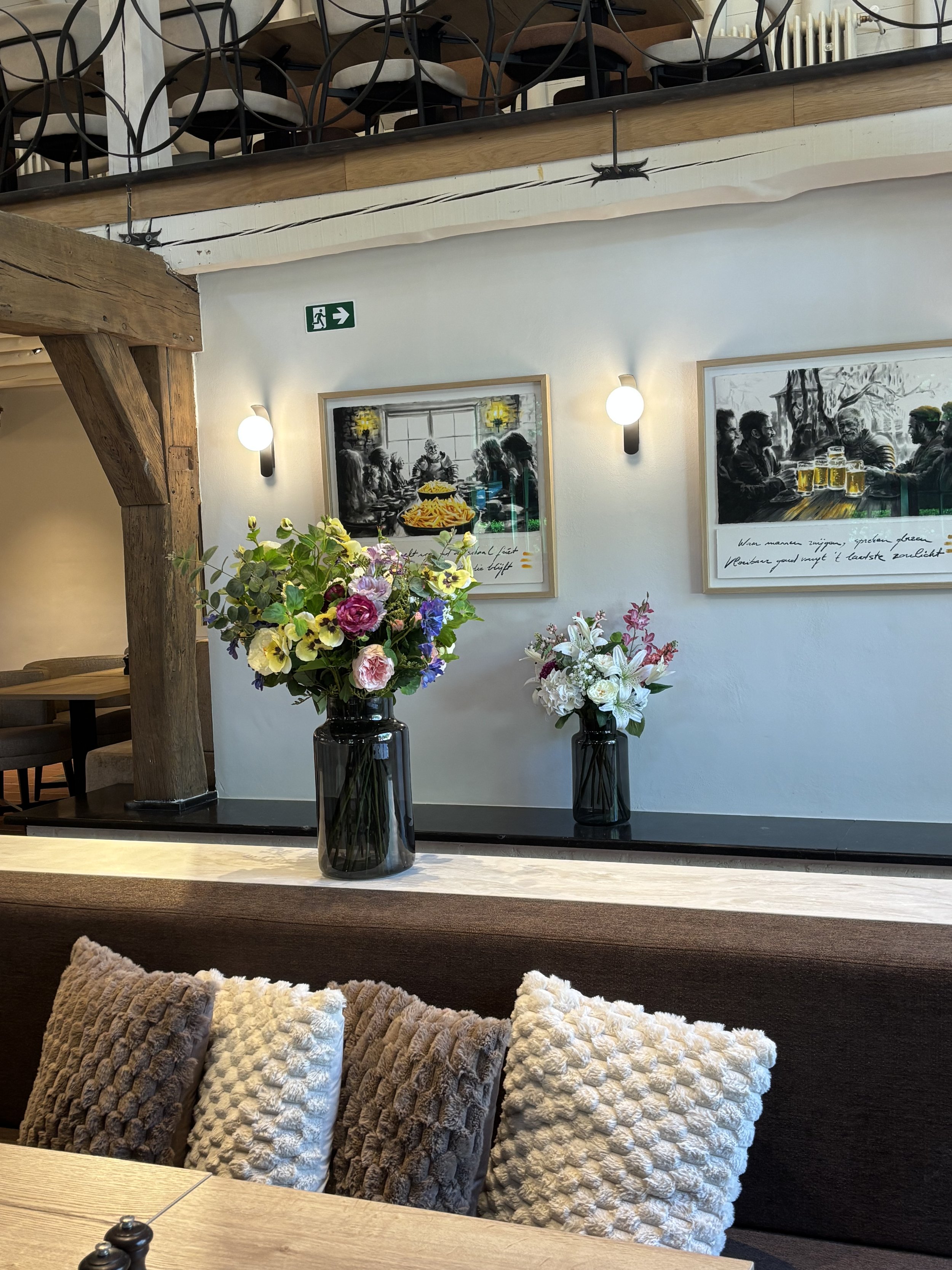 Decorative flower arrangements in glass vases on a table, with framed artwork and seating area in the background of a cozy restaurant interior.