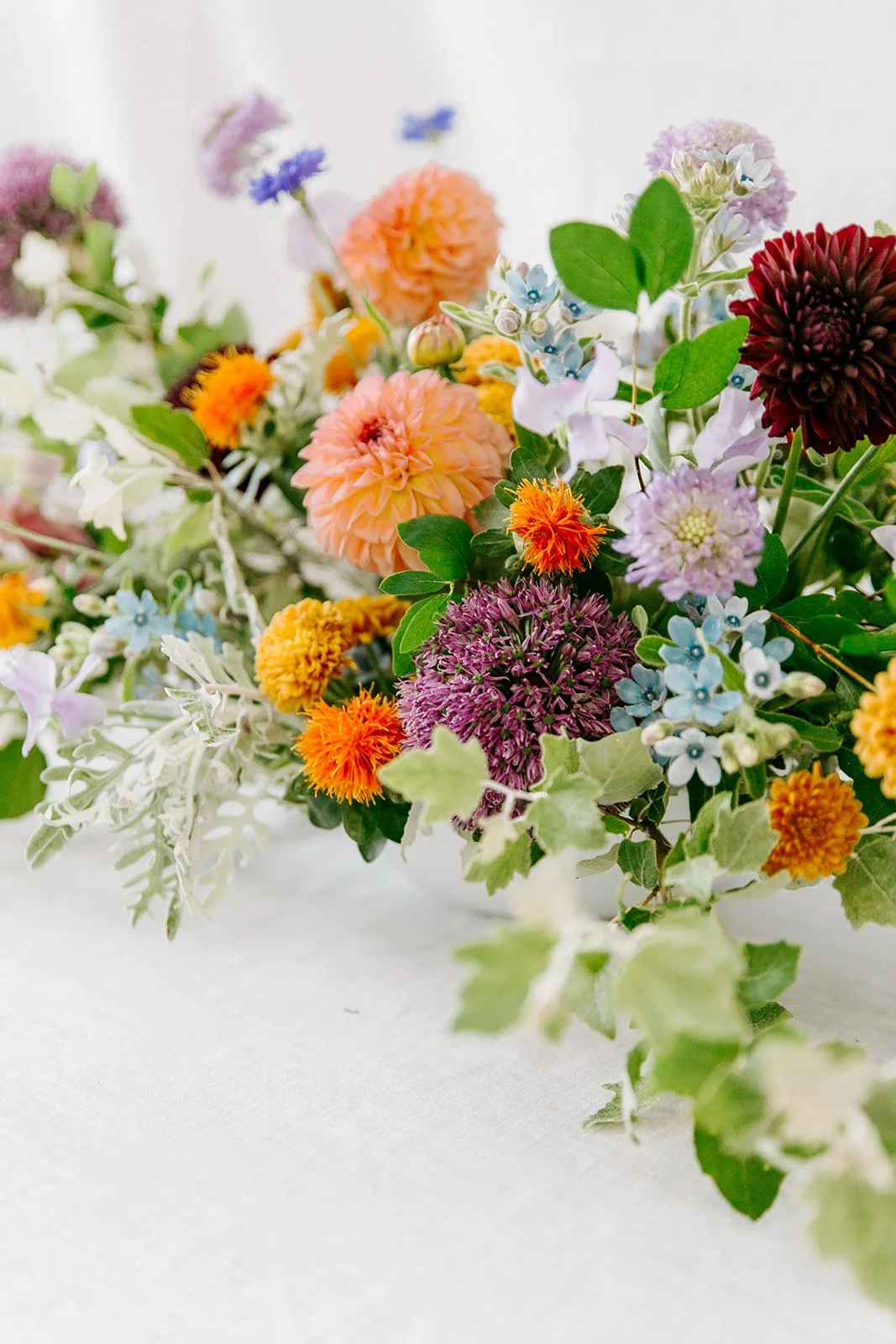 A close up of bright orange, purple, and green florals for a wedding or event table arrangement