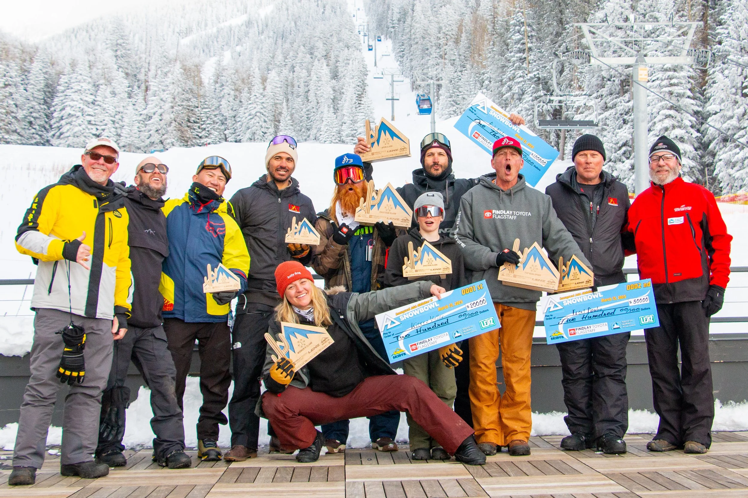 Group of people holding awards and oversized checks at a snowy mountain ski resort.