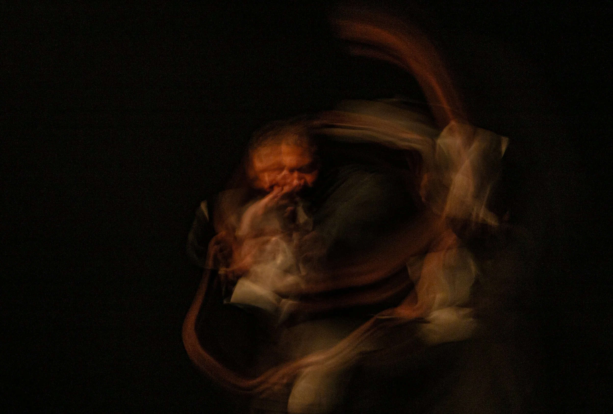 Abstract, blurred image of a man playing the saxophone, with motion trails and dark background.