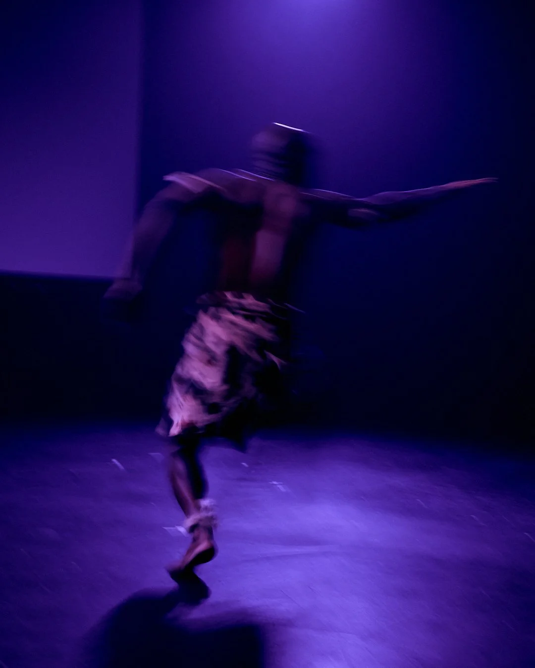 A person dancing in a dark room with purple lighting, wearing camouflage pants and a hoodie, captured in motion.