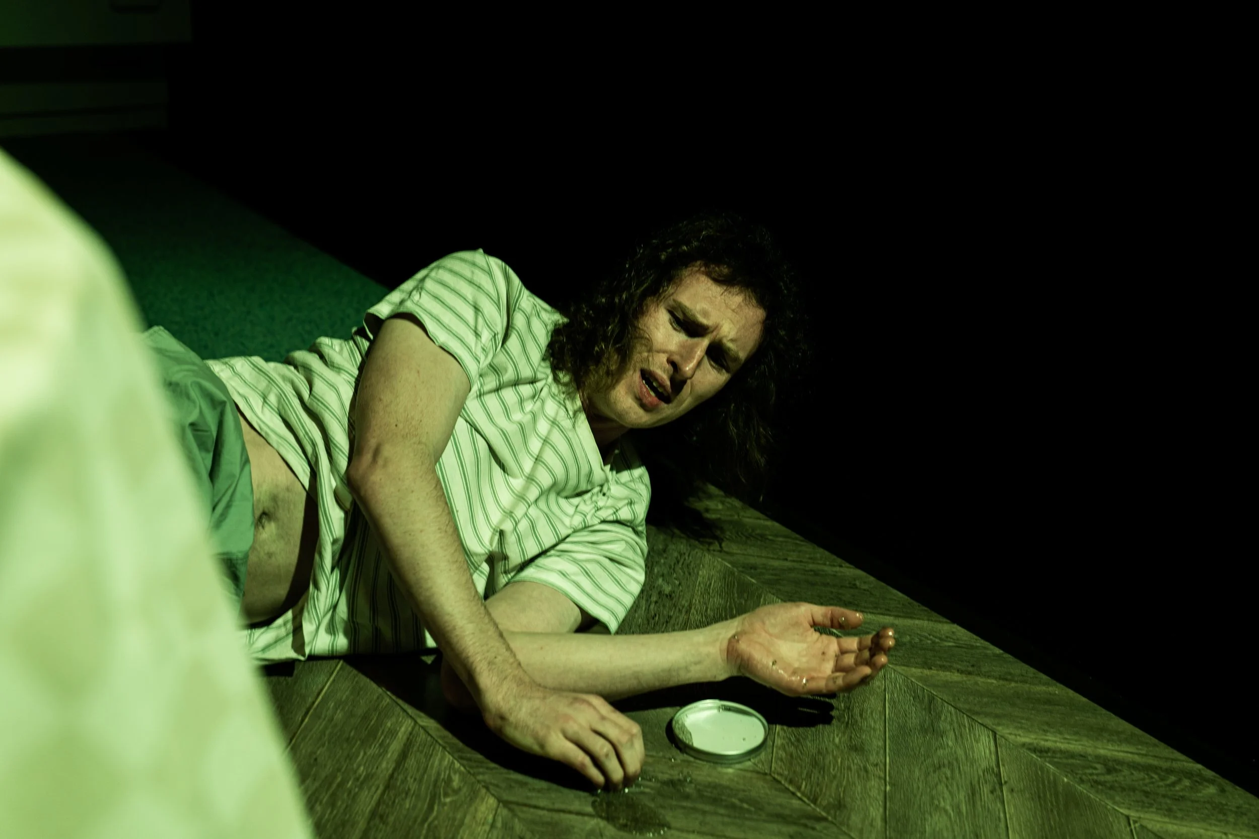 Woman lying on the floor, looking distressed, with a small dish nearby and a dark background.