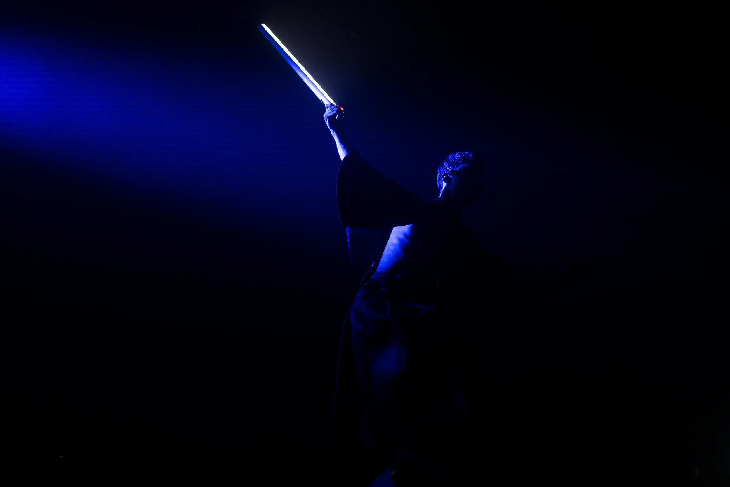 A silhouette of a person holding a glowing blue lightsaber in a dark setting.