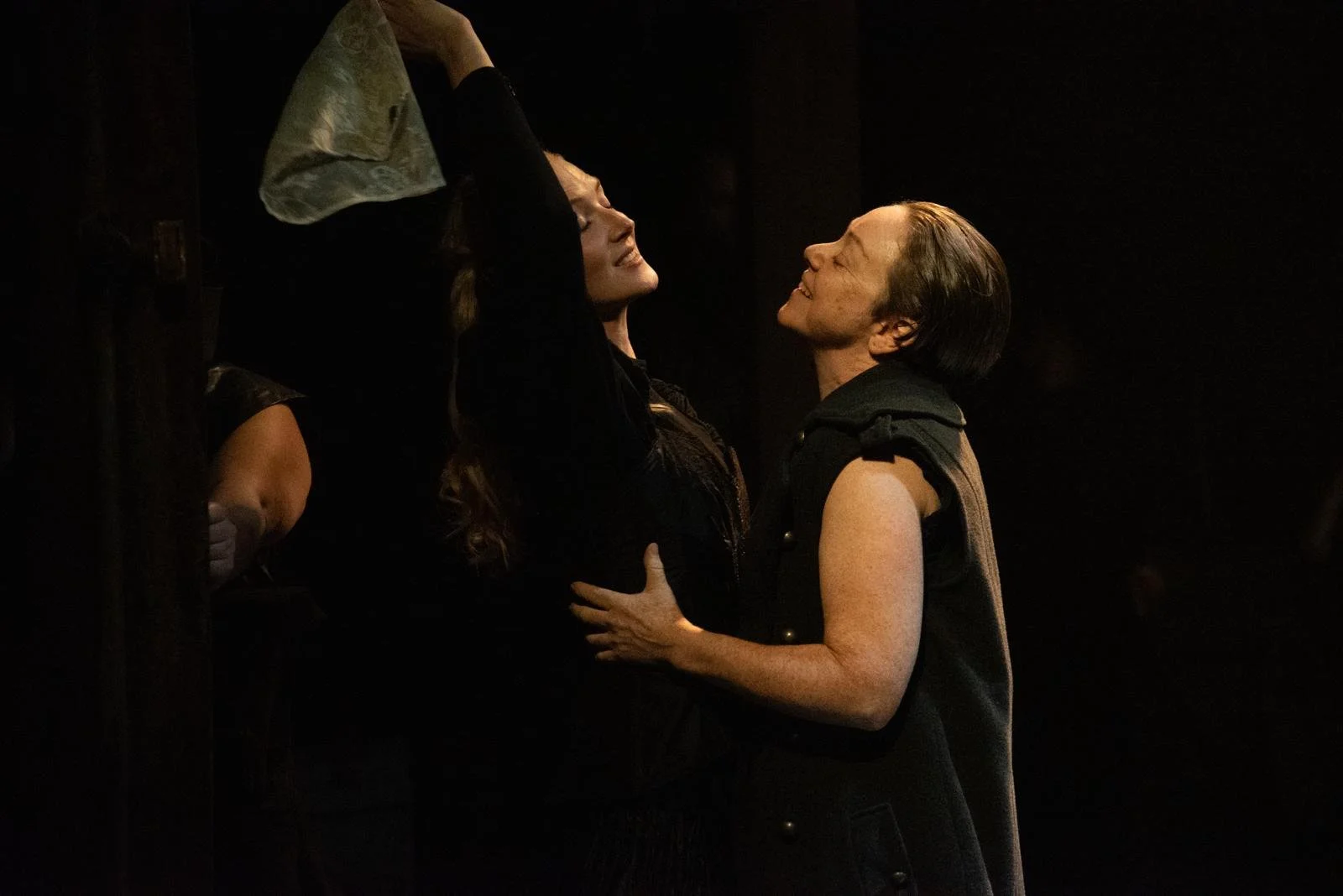 Two women are smiling and embracing each other in a dark room. One woman has her arms raised, and they are looking into each other's eyes, sharing a happy moment.