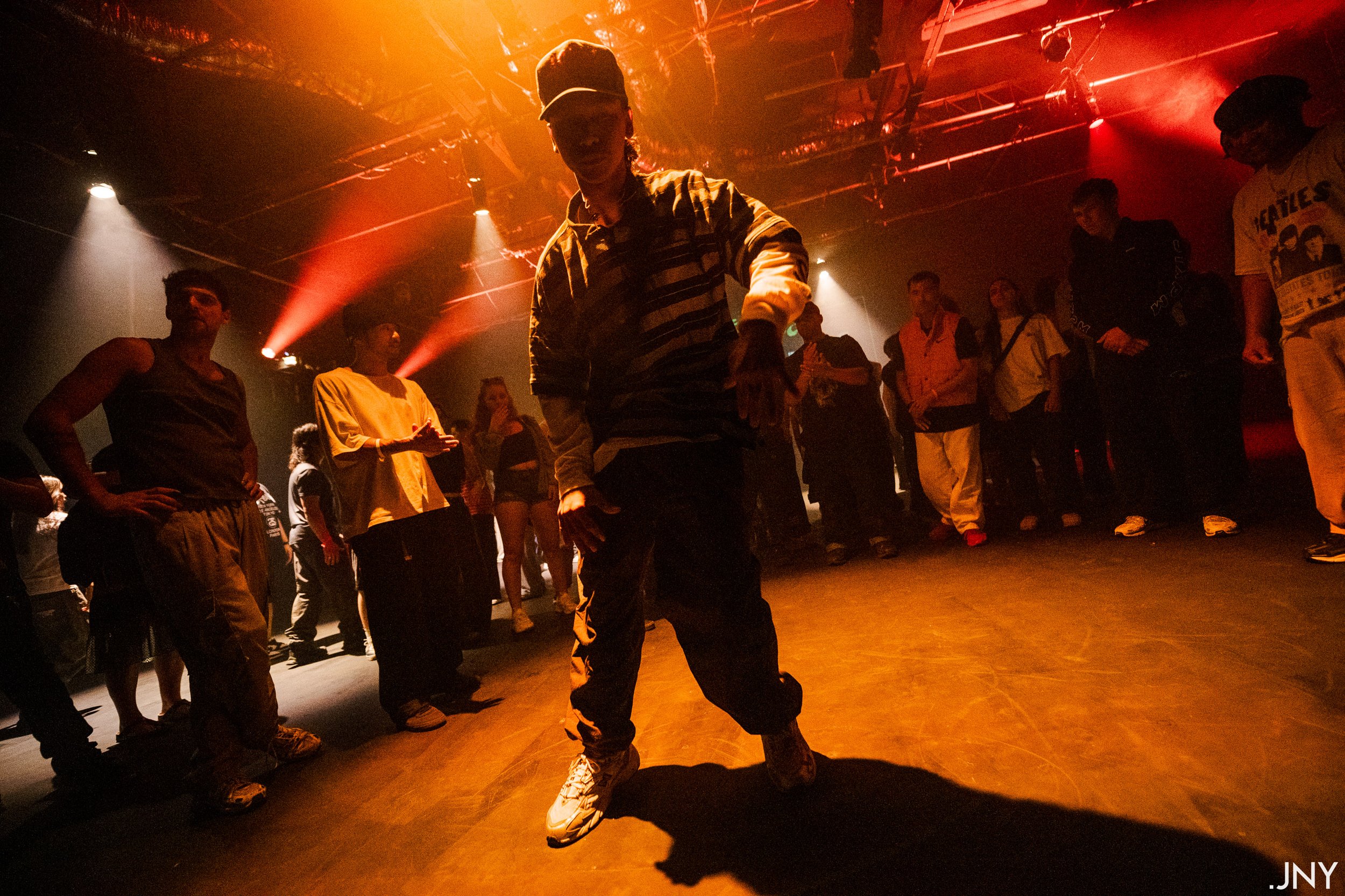 Person dancing on a dimly lit stage with an audience watching, colorful stage lights and smoke effects in the background.