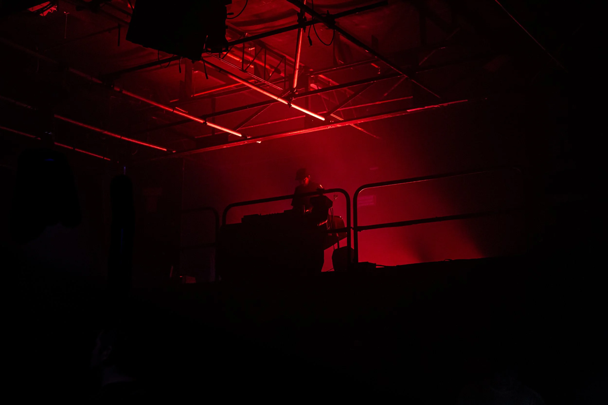 A DJ performing on stage in a dark venue illuminated by red lighting and neon lights.