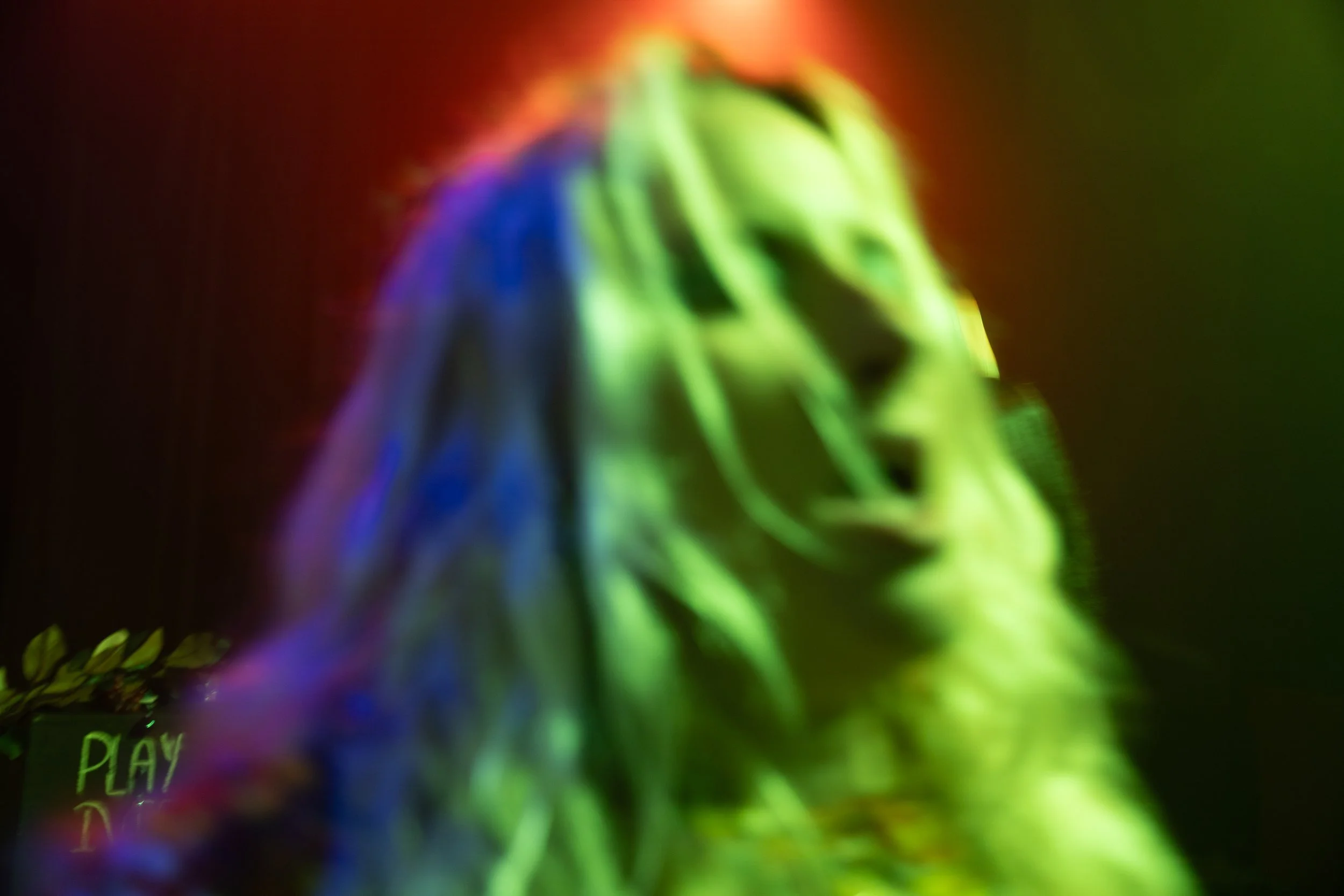 A blurry, colorful image featuring a person's face with rainbow-colored lighting effects, and the word 'PLAY' visible in the background.