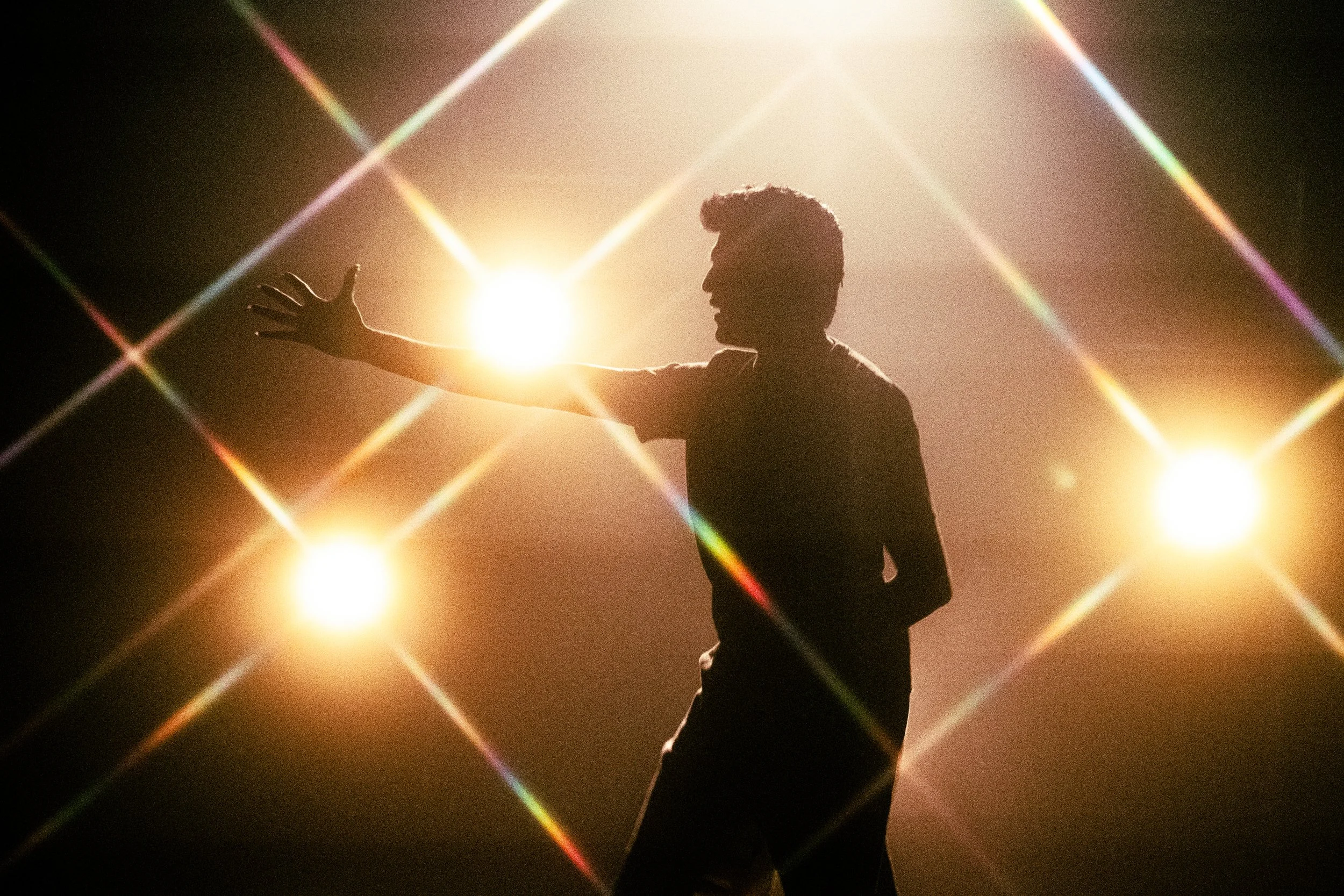 Silhouette of a person reaching out with bright stage lights creating a starburst effect around them.