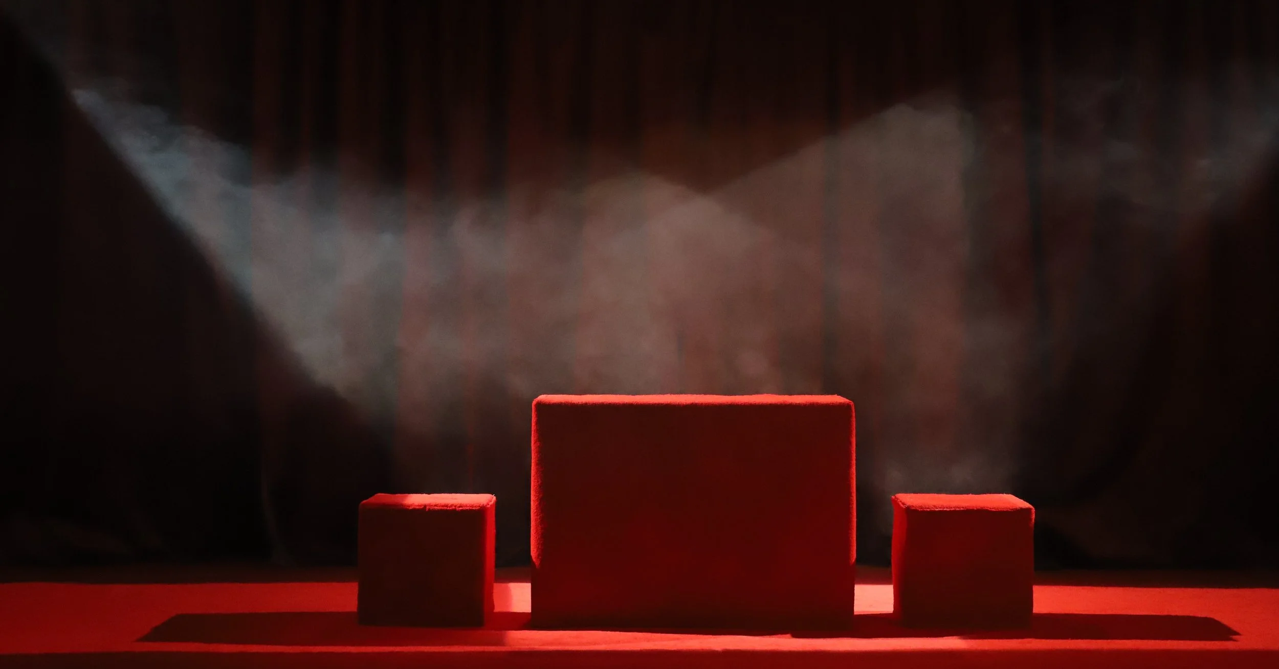 Three red rectangular blocks of varying sizes arranged on a red surface with a dark background.