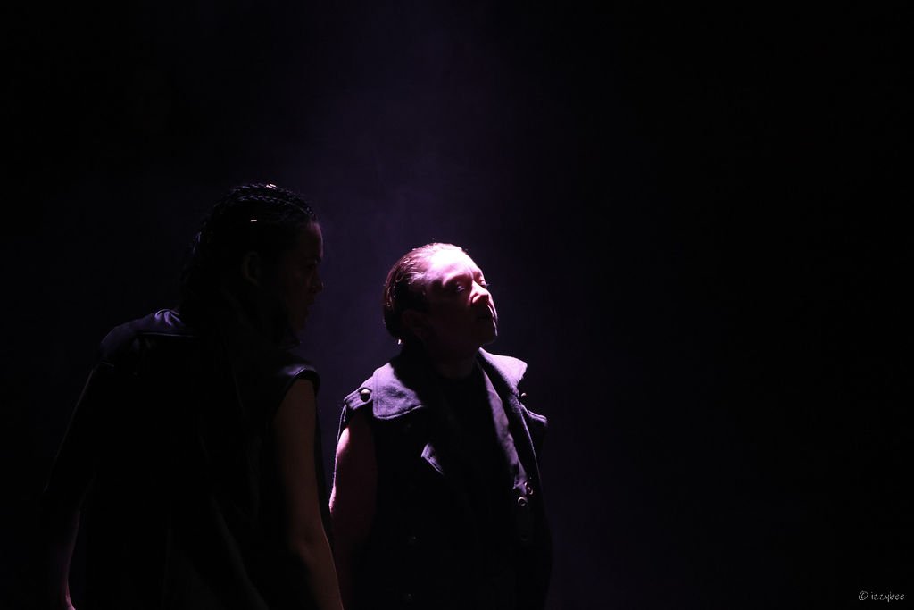 Two people in a dark setting with a bright light focusing on them, creating a dramatic silhouette effect.