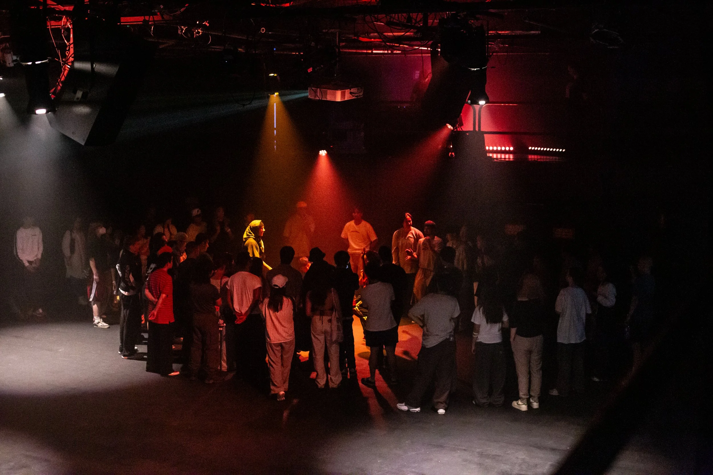 Group of people on a dark stage with red and yellow spotlight lighting.